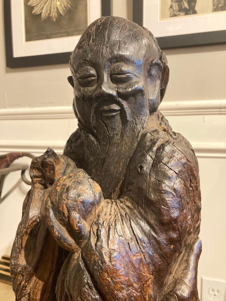 Beautifully carved root sculpture of Shou Lao, the Taoist god of longevity, shown with his serene and content expression, long beard and flowing robes with a pilgrims flask on his belt. In his left hand he holds a peach, his right hand is missing.