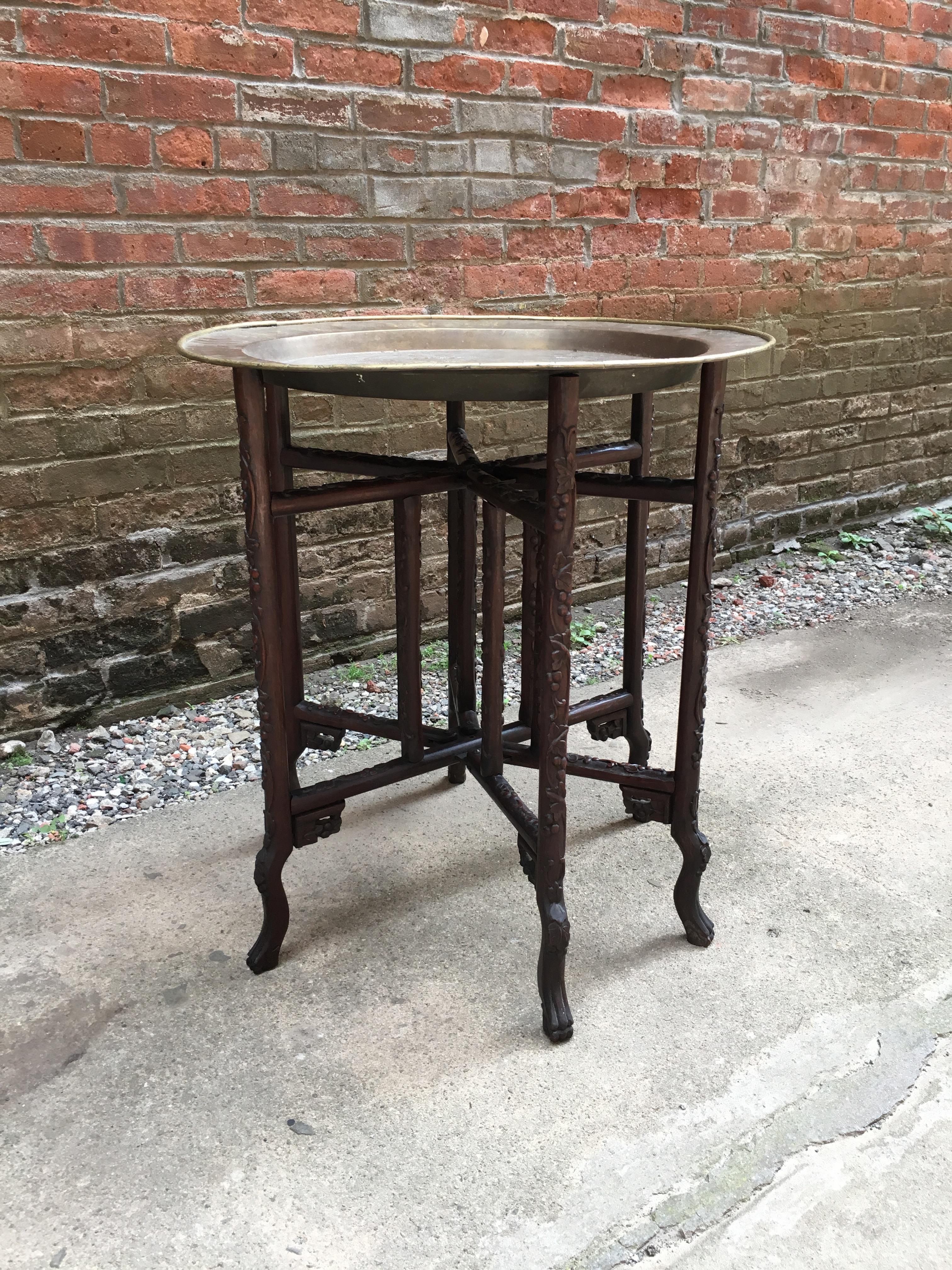 Exquisitely carved and chased brass Chinese folding table. The rosewood base is a raised floral motif and the chased brass charger is decorated with 16 individual flora and fauna scenes flanking a large character with a rolled edge, 19th century.