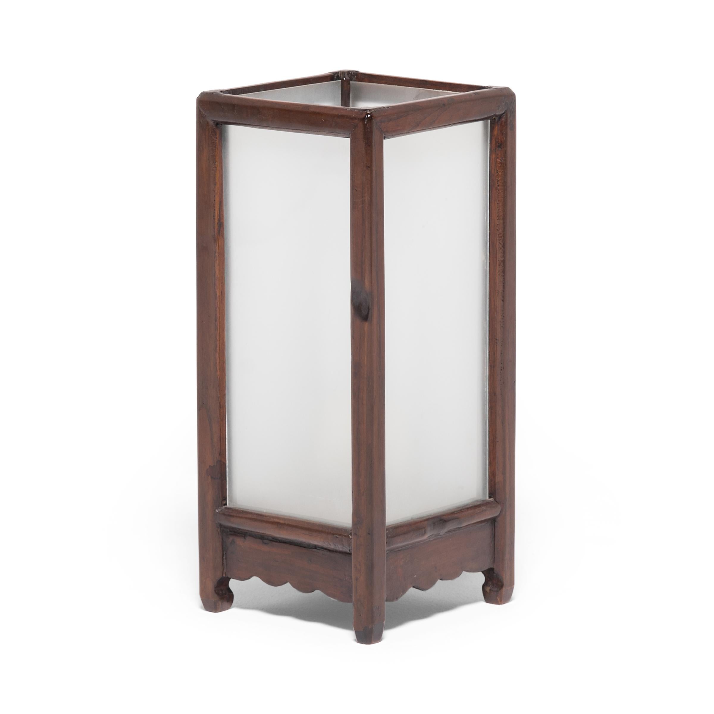 Framed in hand carved rosewood, this 19th century tabletop lantern casts a soft glow through frosted glass. Exemplifying the simplicity found in Chinese furniture of the same era, this lantern illuminates modern interiors with a refined form that