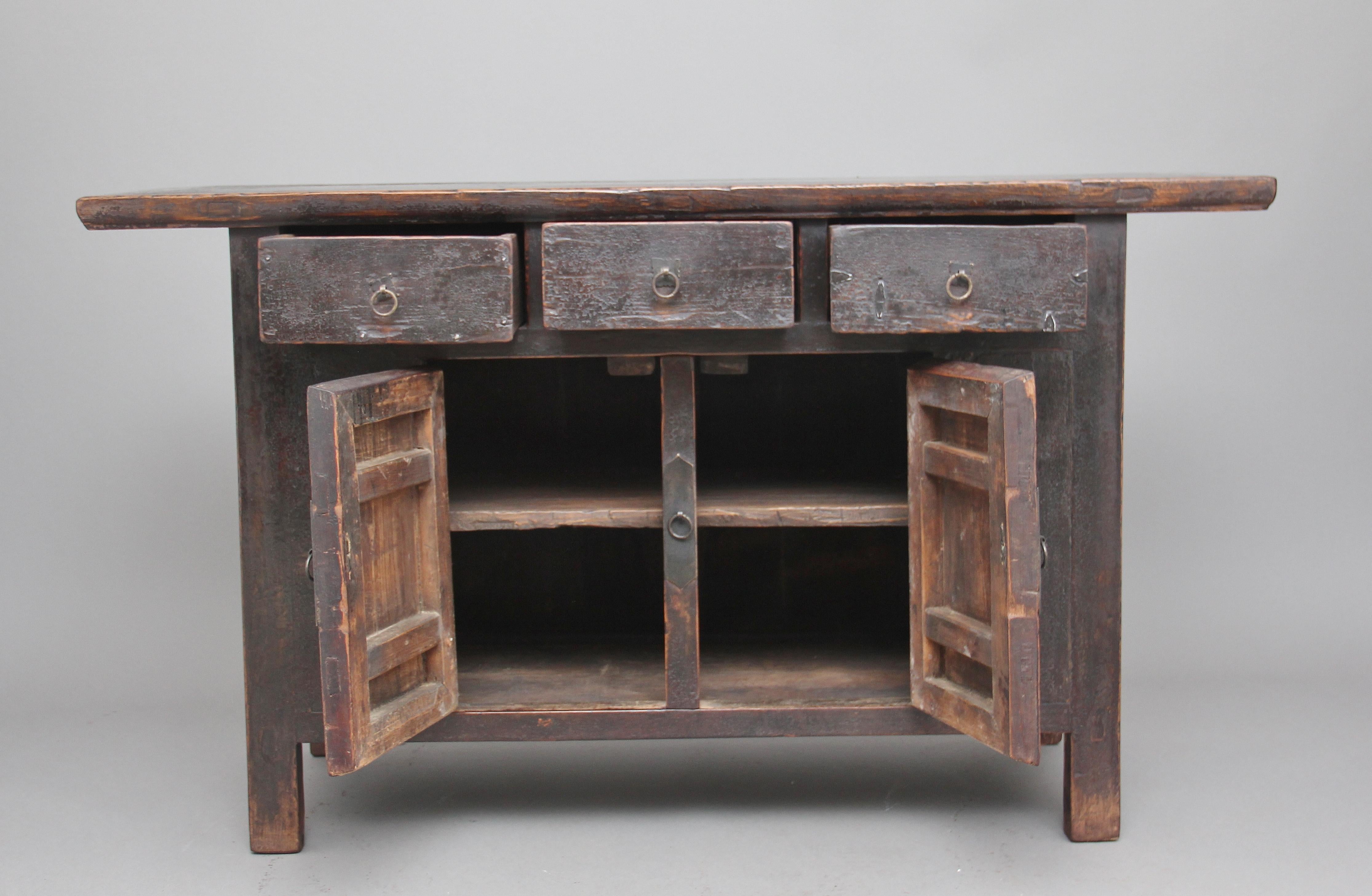 19th century Chinese rustic elm dresser in the traditional shape and style, the cabinet having three drawers with original ring pull handles above a two-door cupboard opening to reveal a single fixed shelf inside standing on square legs, circa