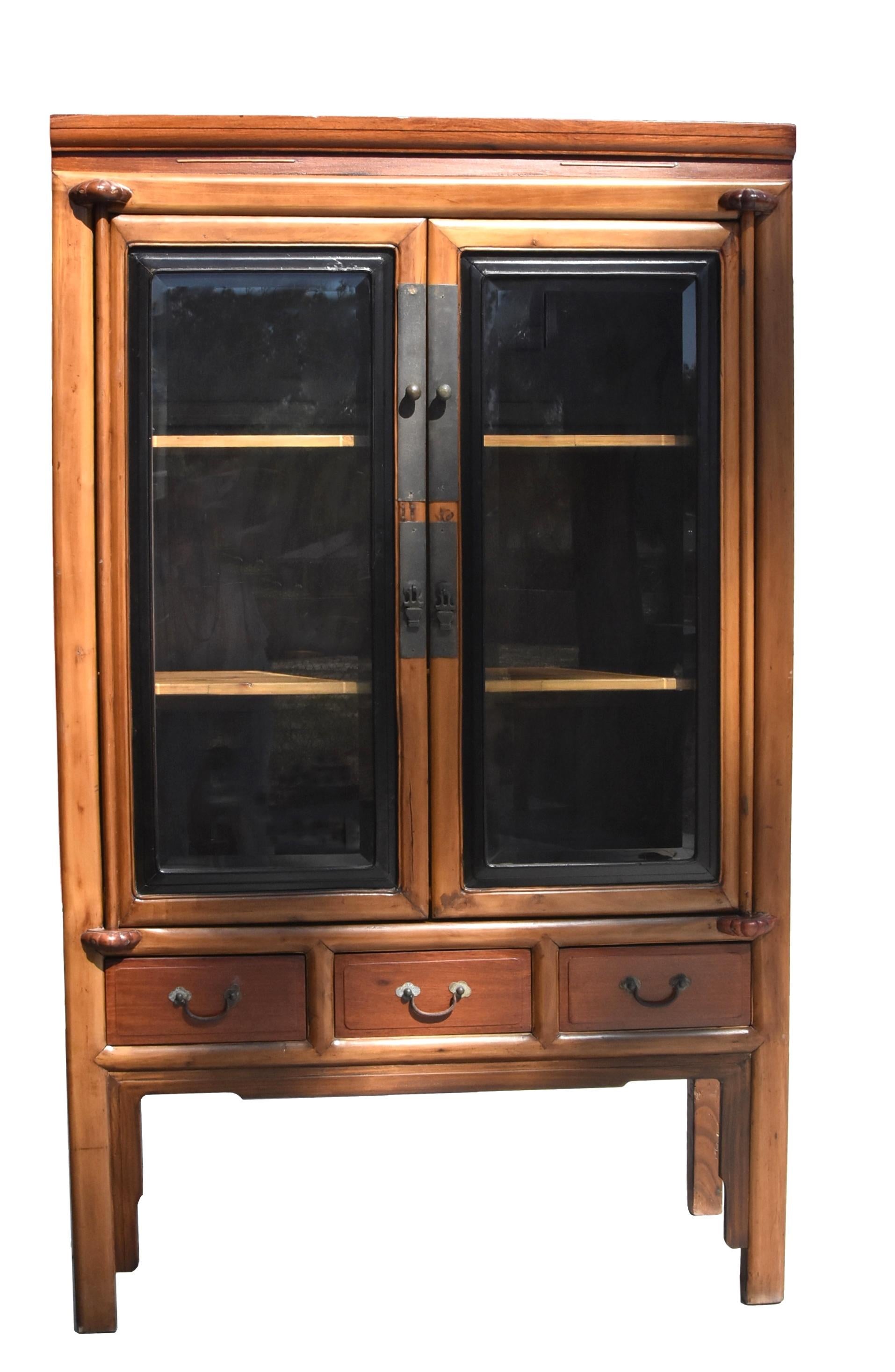 A late 19th century solid wood Chinese scholar's cabinet with glass doors and removable shelves. The glass doors with elegant black lacquered frames are mounted on dowels adorned with carved lotus. Above the doors a waist below the top facade