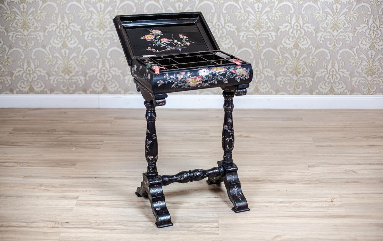 We present you a neat sewing table from the late 19th century.
This piece of furniture is covered in black lacquer with inlays of mother-of-pearl.
The rectangular apron can be opened from the top. The inside is multi-layered and there is a removable