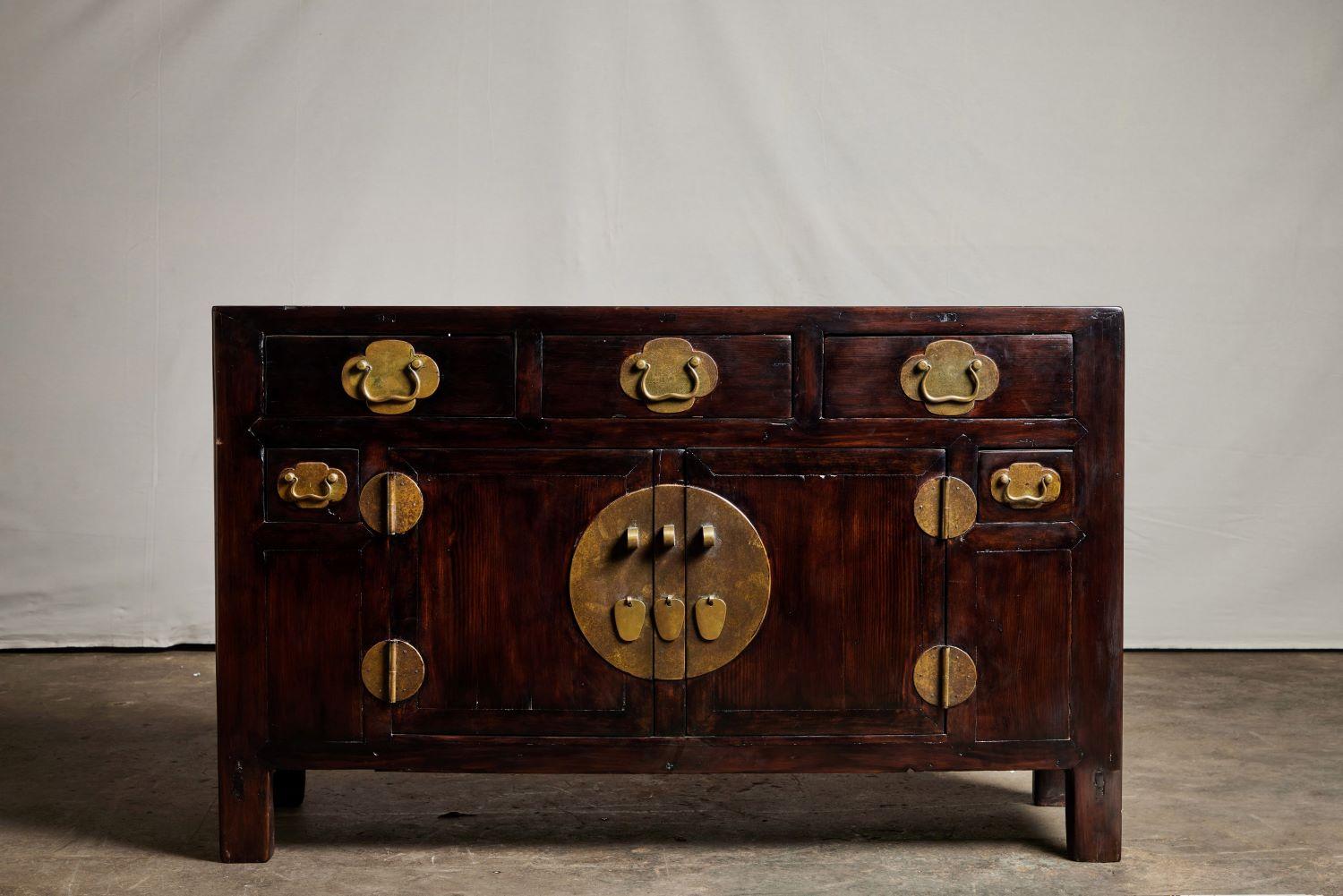 A 19th century narrow Chinese yellow pine cabinet featuring very fine grain and brass hardware. The cabinet has a set of three drawers on the upper portion with one large cabinet underneath it. The large cabinet features a brass escutcheon and the