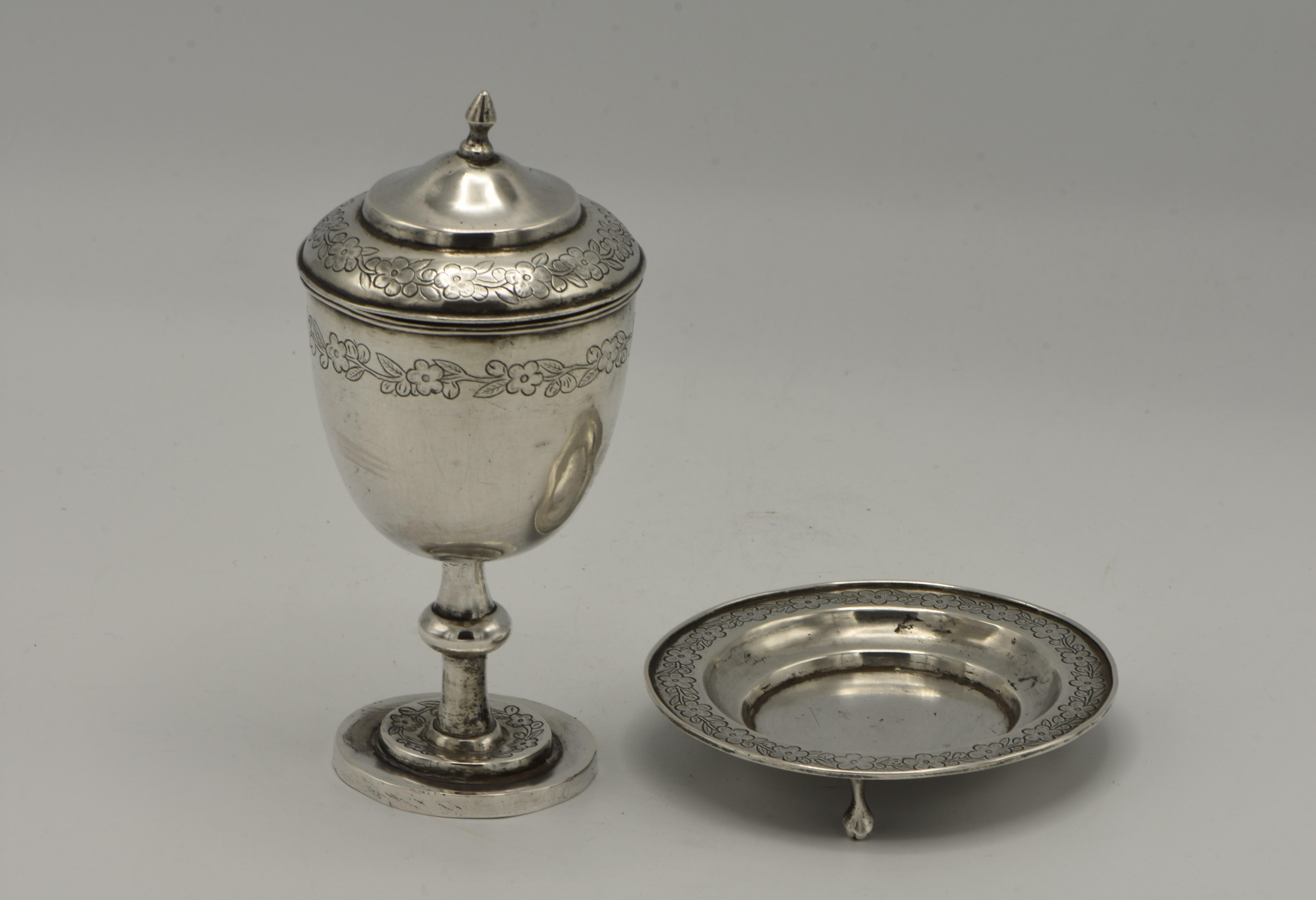 Chinese export silver covered Kiddush cup, 19th century. 
Round bowl on baluster stem mounted to stepped and flat circular foot. Double domed cover with pointed finial. Engraved bands of imbricated leaves. Comes with the original footed saucer with