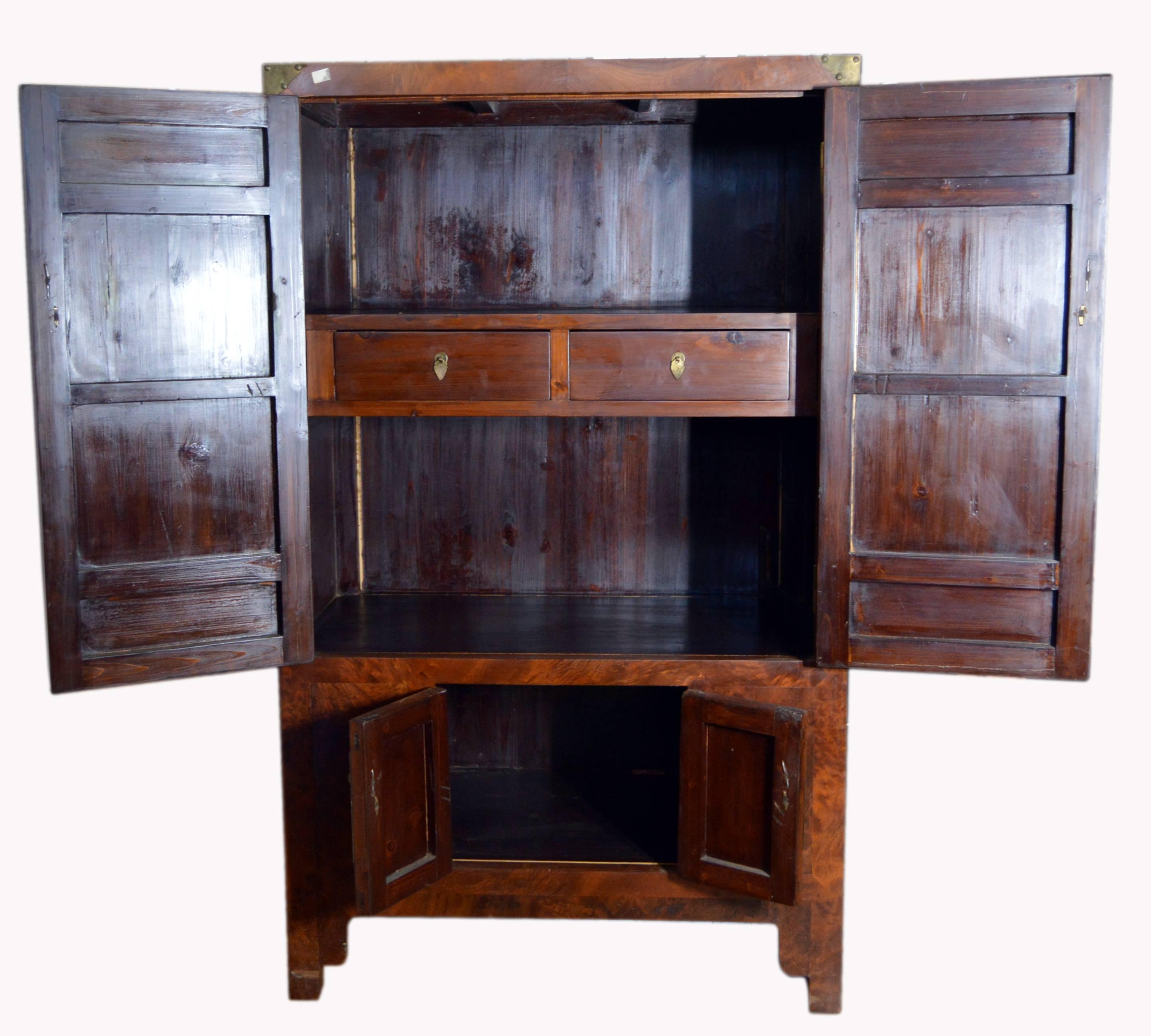 A Chinese 19th century four-door stained burlwood armoire with inner drawers and brass hardware. This exquisite Chinese armoire features a linear silhouette, adorned with two large doors in its upper section, accented with a large round brass plate