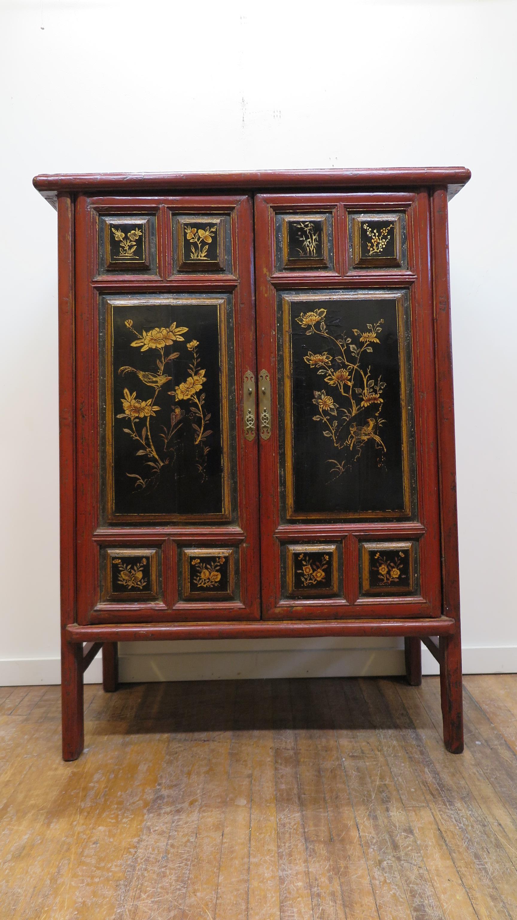 19th century painted tapered Chinese cabinet. Having elaborate panels with gilt painting and raised moldings. Warm red lacquer adorned with black lacquer and gilt painting. Framing the panels recessed into the molding are remnants of crushed