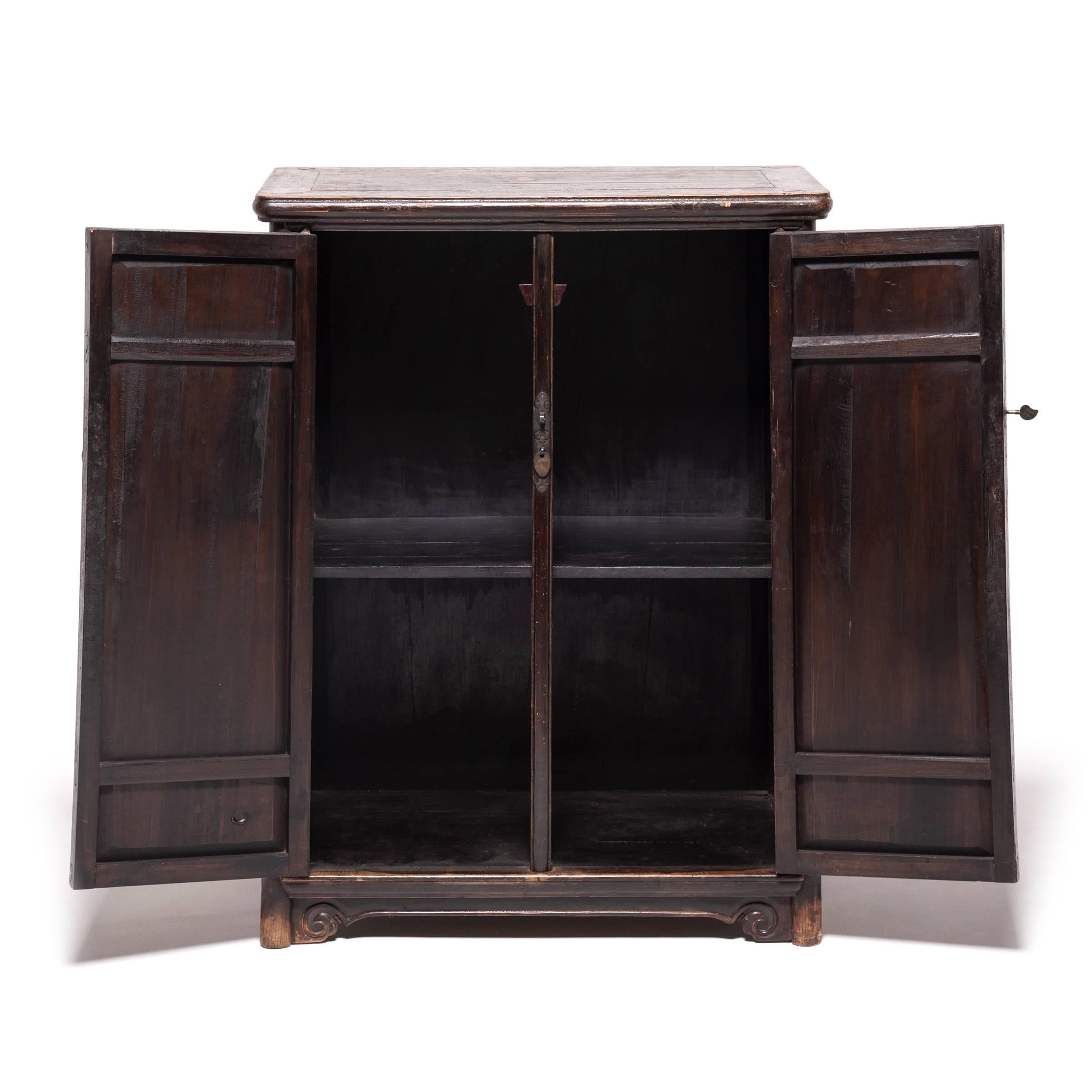 Inspired by the clean simplicity of Ming-dynasty furniture, this tapered cabinet showcases the rich warmth of natural elmwood. Simply accented with rounded corners and subtle cloud scrolls at the feet, the cabinet features brass hardware in the form