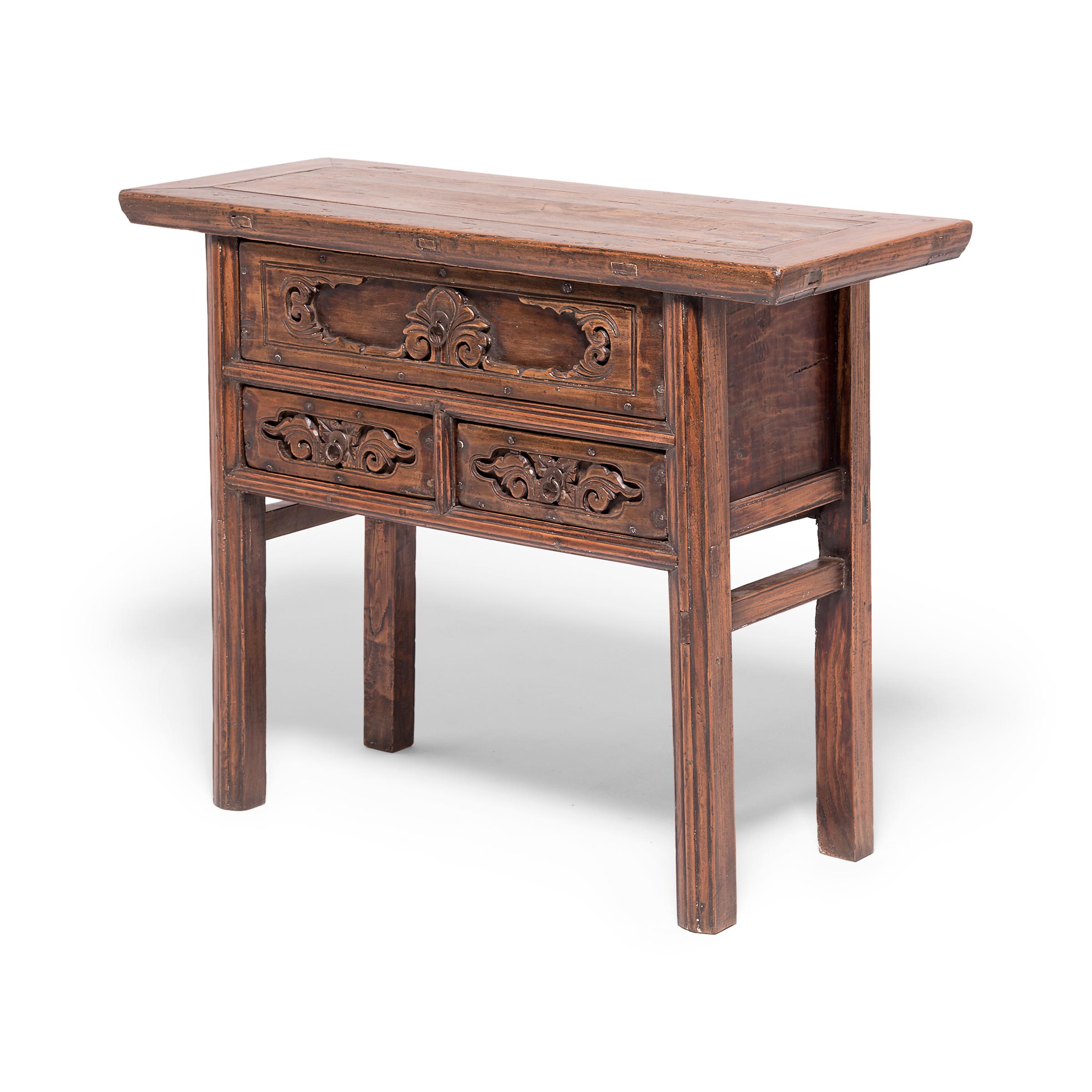 Originally used as an altar table, this beautifully carved table displays intricate flower motifs on its three drawers. Made of northern elmwood in China's Shanxi province, the 19th century console table balances its intricate ornamentation with