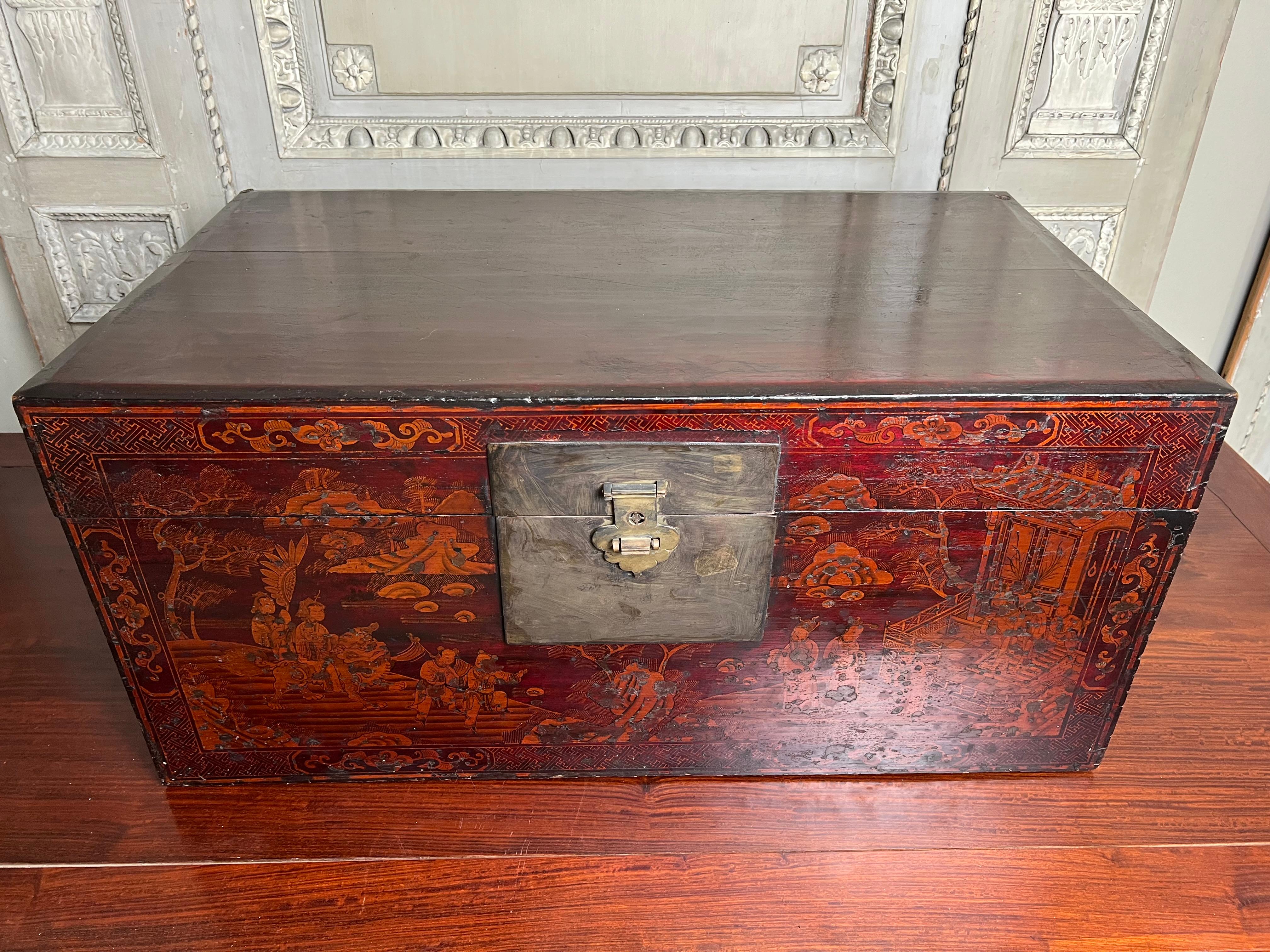 A 19th century Chinese red lacquered trunk with gilt decoration depicting a court scene with mountains and foliage.  This highly decorative trunk is very functional and could be used as a coffee table, under a console or placed on a stand for a side