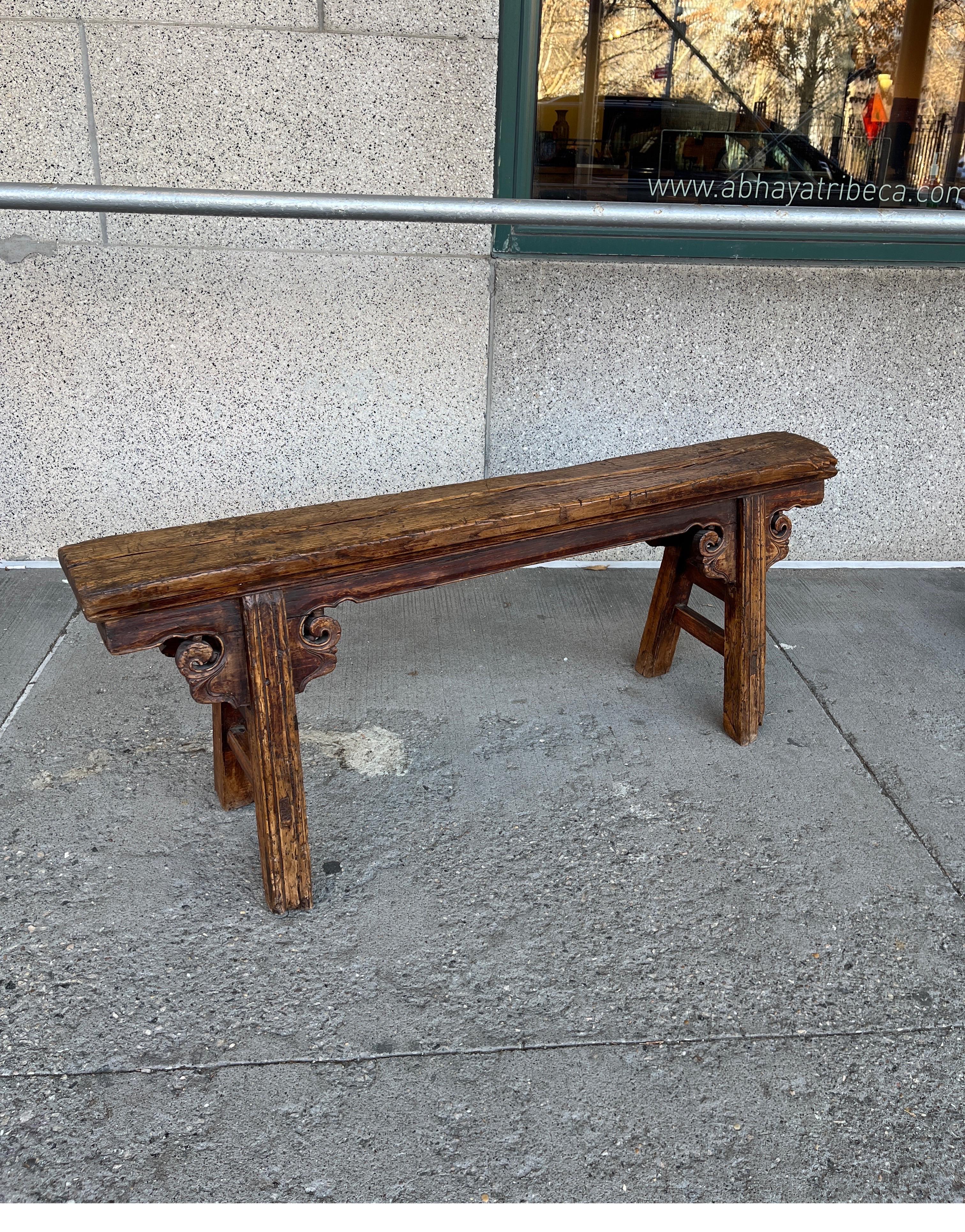 A truly Classic antique Chinese two person bench with great patina and simple design. Highlighted by two simple expertly carved decorations, this entirely handmade elm bench exhibits its 150 years of use during the Qing Dynasty, the Republic Period