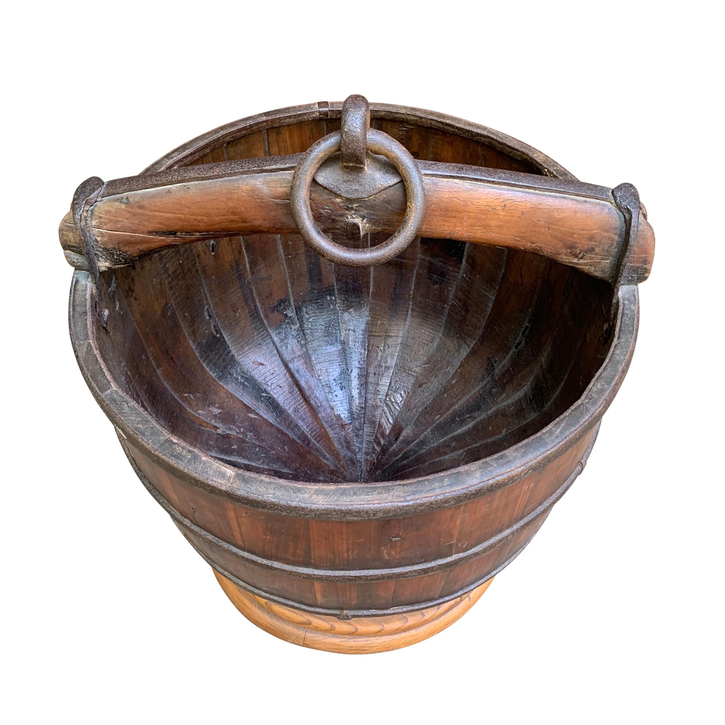 A fantastic 19th century Chinese wooden water bucket with beautiful heavy iron straps and a handle with an in iron ring that was originally used to raise and lower the bucket. The bottom tapers so a turned wood stand was created so that the piece
