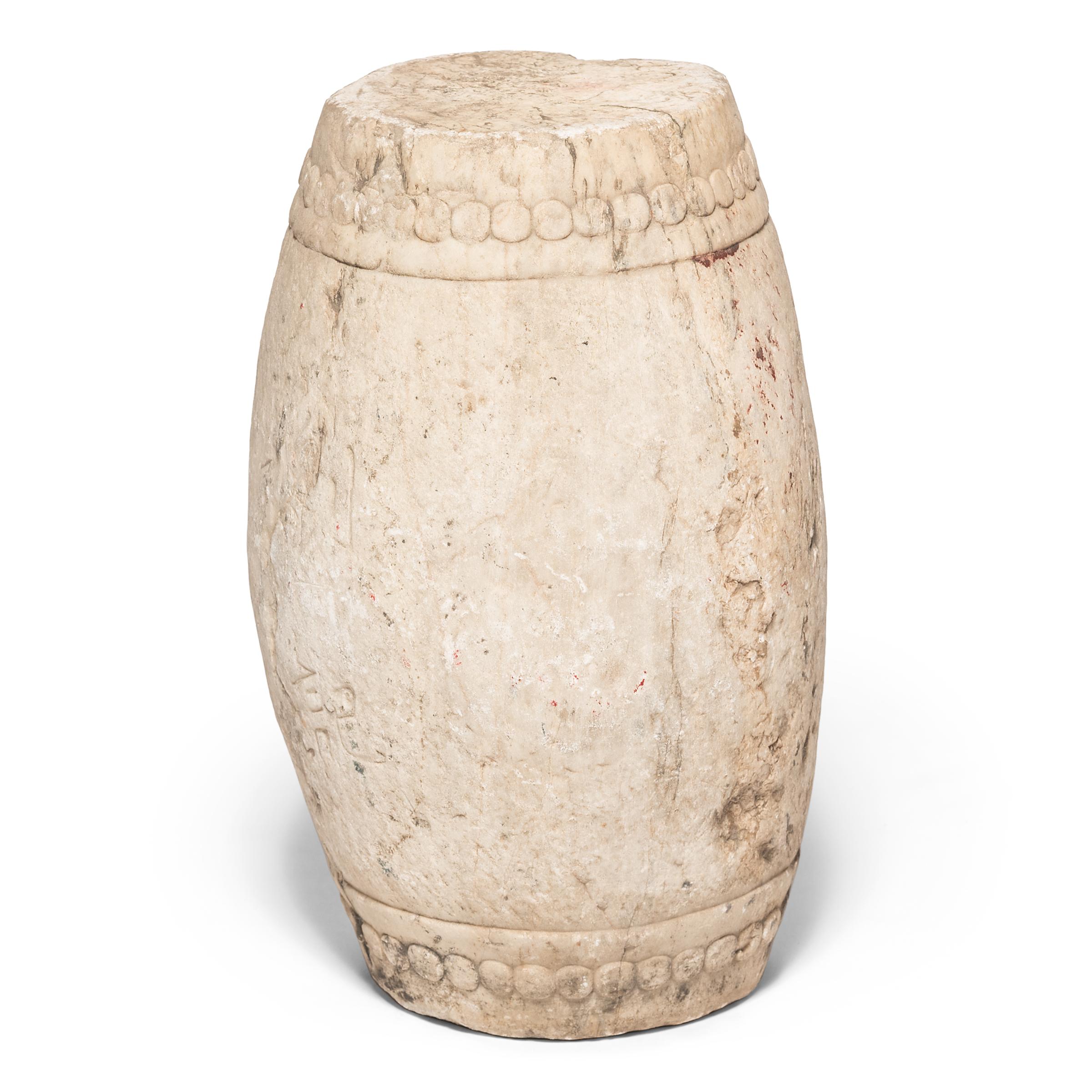 Carved from a single block of white marble, this early 19th-century garden stool has a traditional drum-form shape. Ringing both its top and bottom, a pattern of boss-head nails imitates those used to stretch a skin on an actual drum. The stool