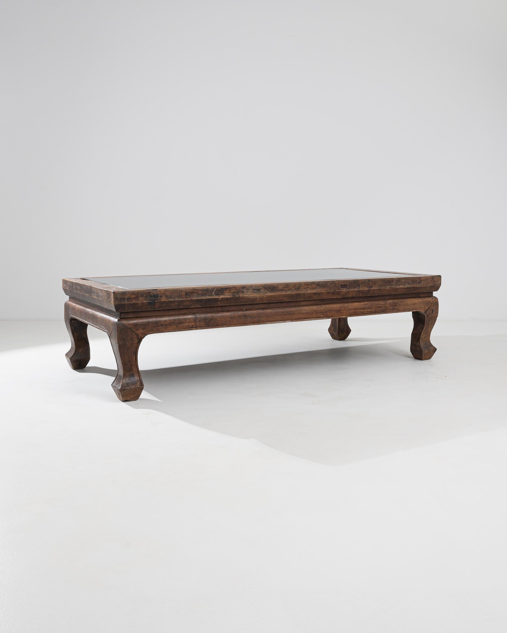 A 19th century Chinese coffee table made from wood and a glass top. This enormous coffee table radiates both a commanding presence as well as a cozy aura. Its thick lumber and gentle curves indicate a sense of confident and keen-eyed craftsmanship.