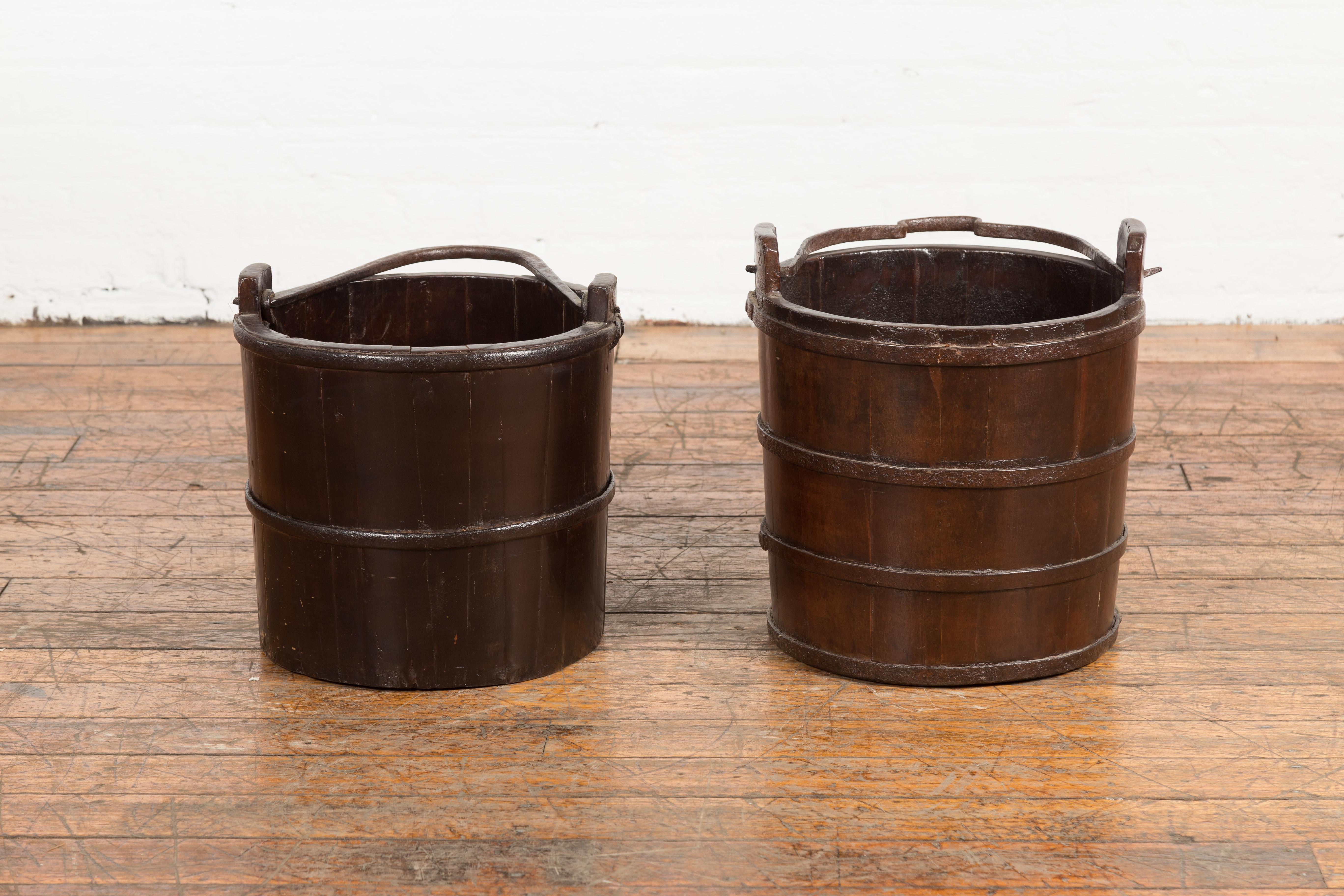 Two antique Chinese Qing Dynasty period wooden dark brown lacquered well buckets from the 19th century, with large metal handles and horizontal braces, priced and sold individually. These antique Chinese wooden dark brown lacquered well buckets from