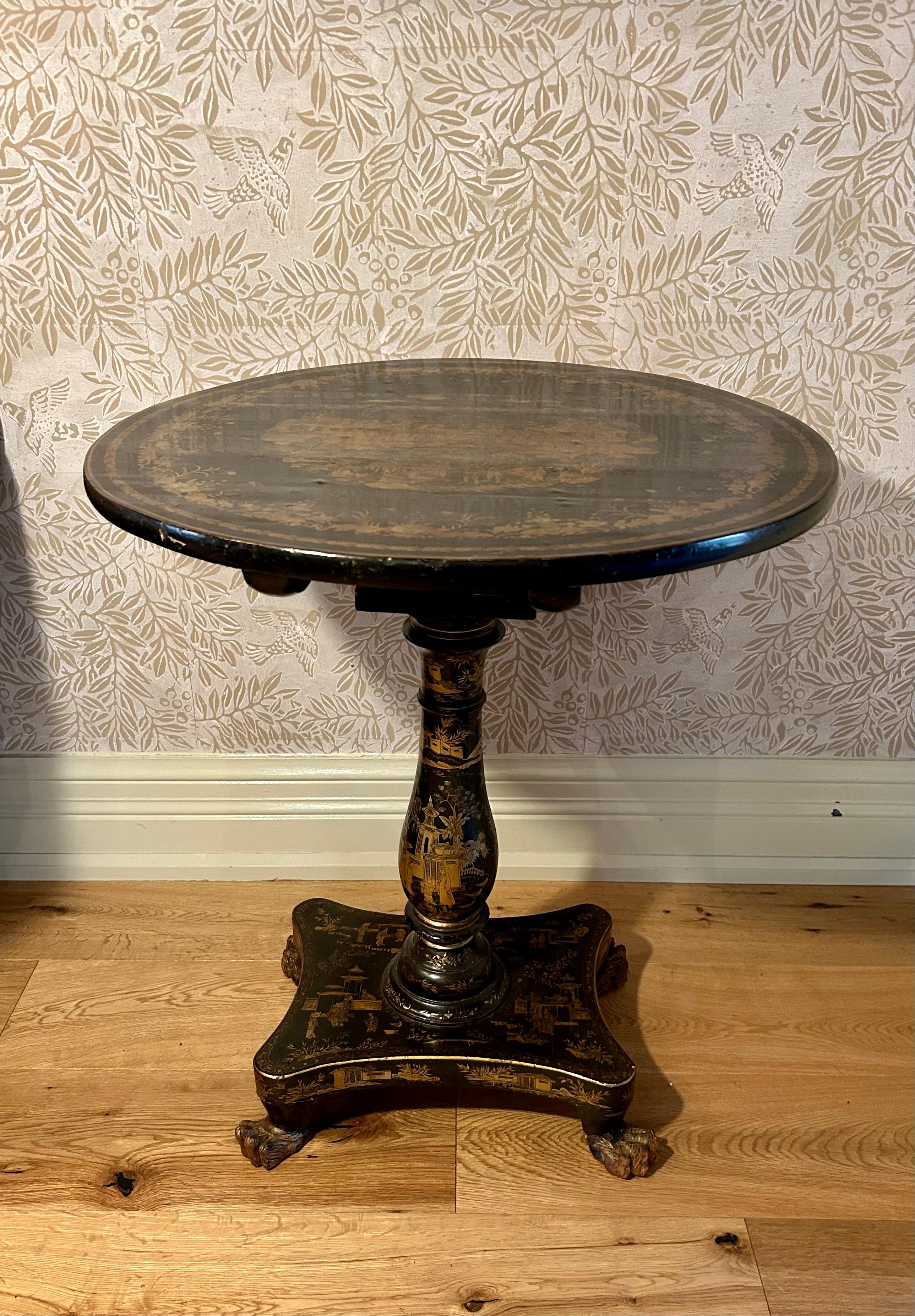This is an exquisite Chinese export tilt-top table with a quatrefoil base and four claw feet. The pedestal is in a baluster shape and the top is round. All in black lacquer with extremely fine gold chinoiserie designs throughout, depicting figures