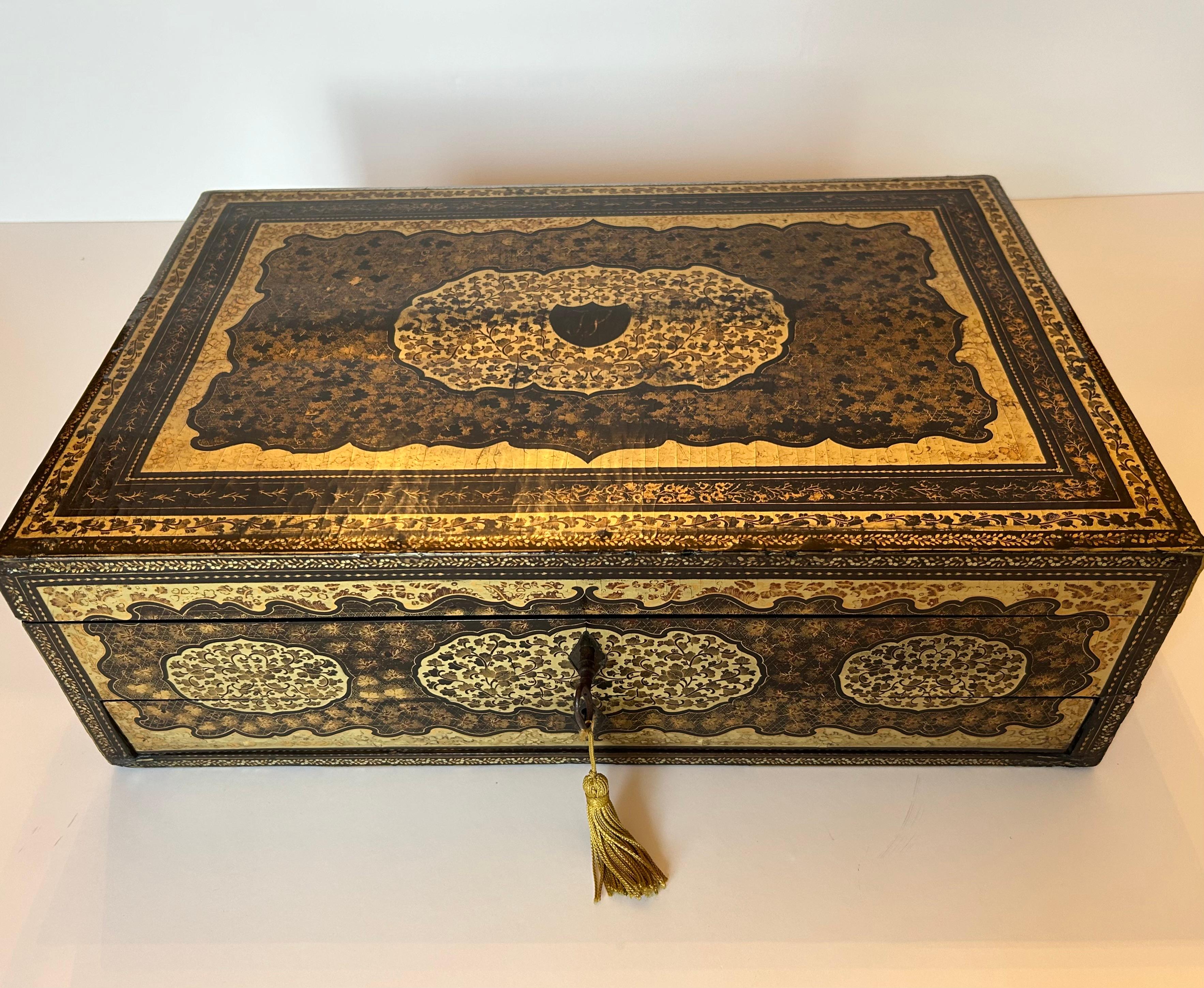 This is a remarkable 19th century lacquered sewing box with multiple compartments on the interior.
The exterior is decorated in elaborate black and gilded motifs including flowers, foliage and grapes. The top portion of the interior is fitted with
