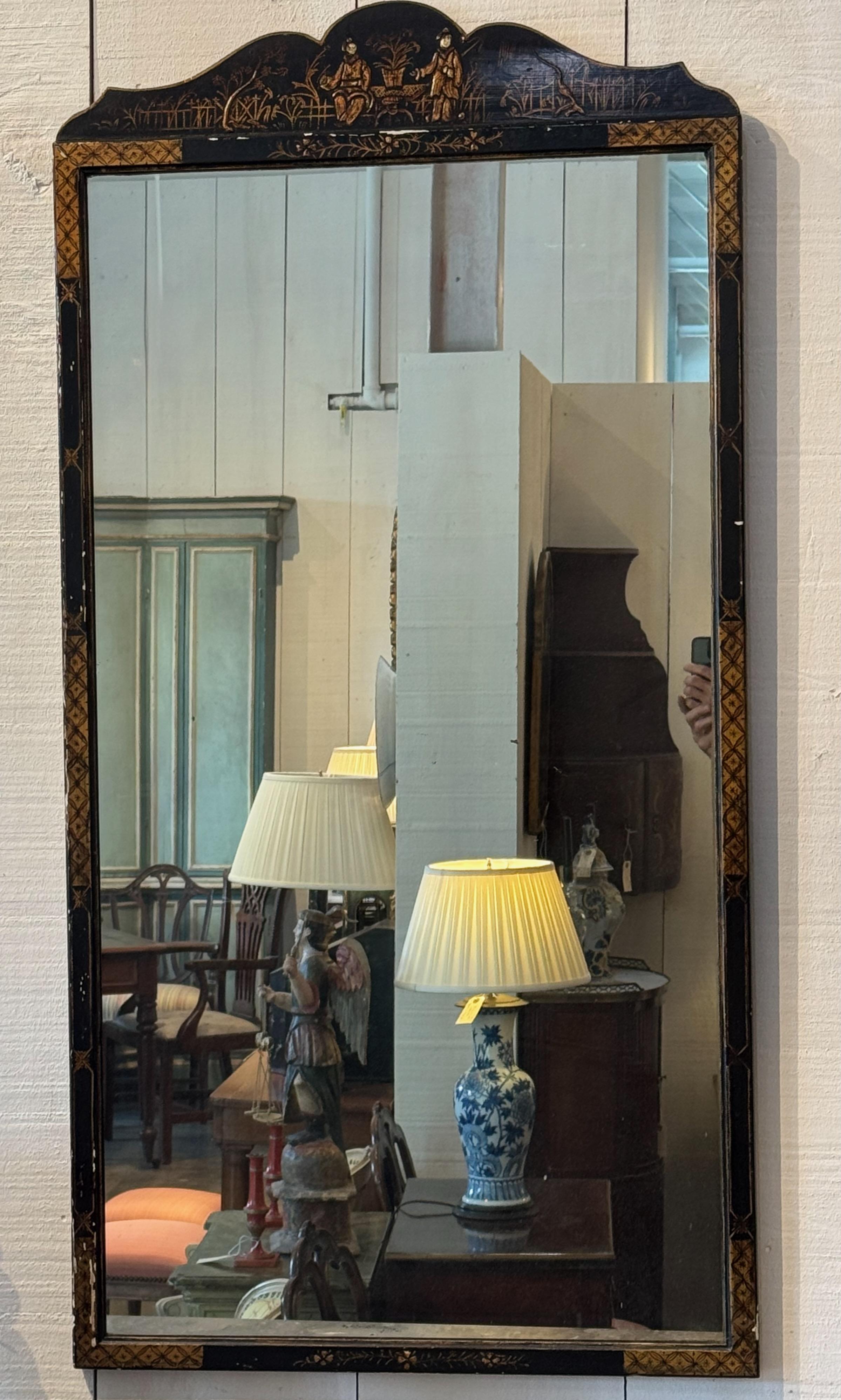 Espejo de pared de Chinoiserie con cresta perfilada y marco pintado de negro decorado con motivos figurados y paisajísticos dorados. El panel superior presenta figuras sentadas y de pie en una escena de jardín, mientras que el borde está ribeteado