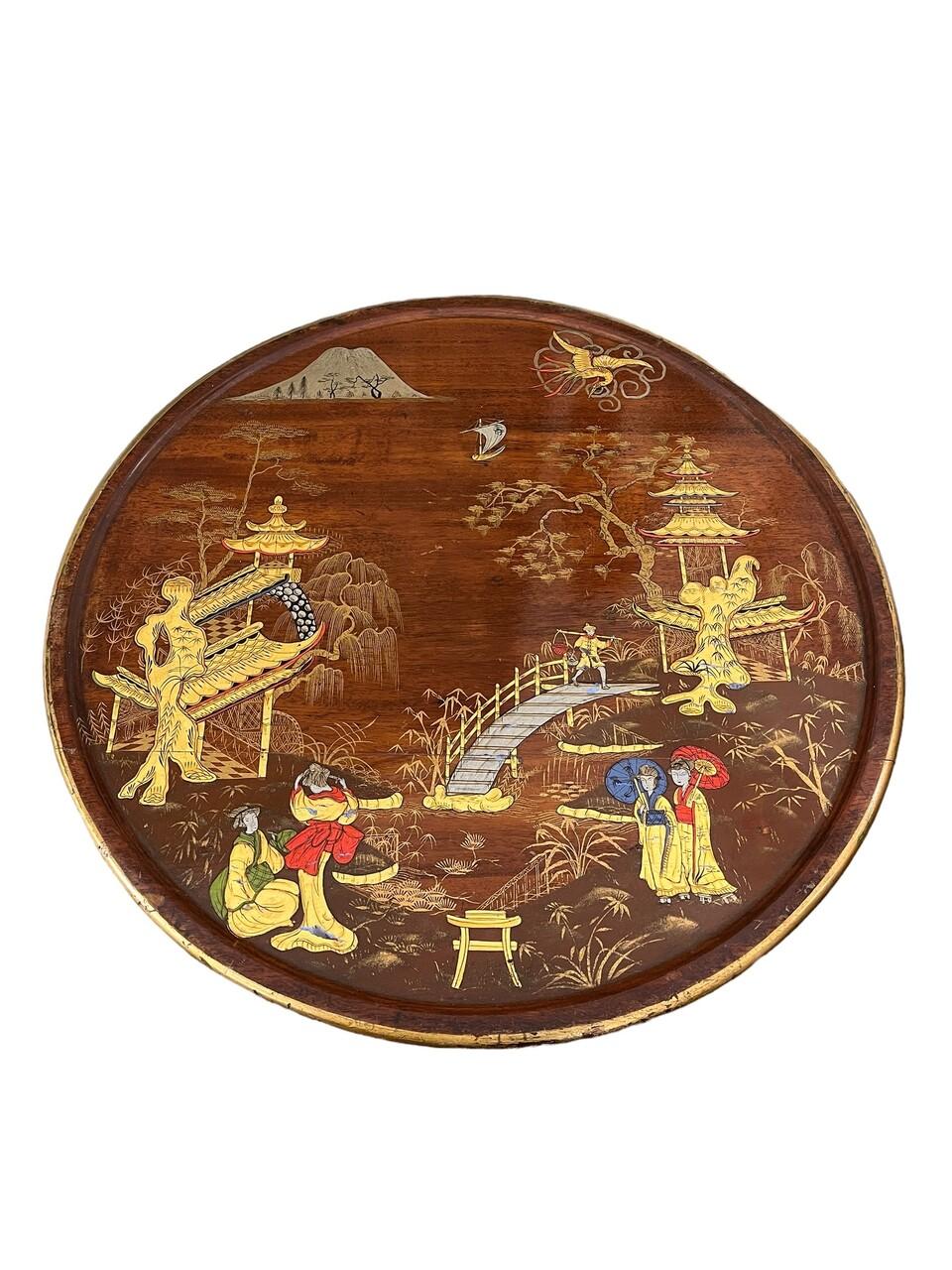 Cette table à vin tripode de style Chinoiserie du 19ème siècle possède une base balustre tournée et d'élégants pieds descendants avec des patins. Sa surface est ornée d'une scène de village méticuleusement peinte à la main, complétée par un