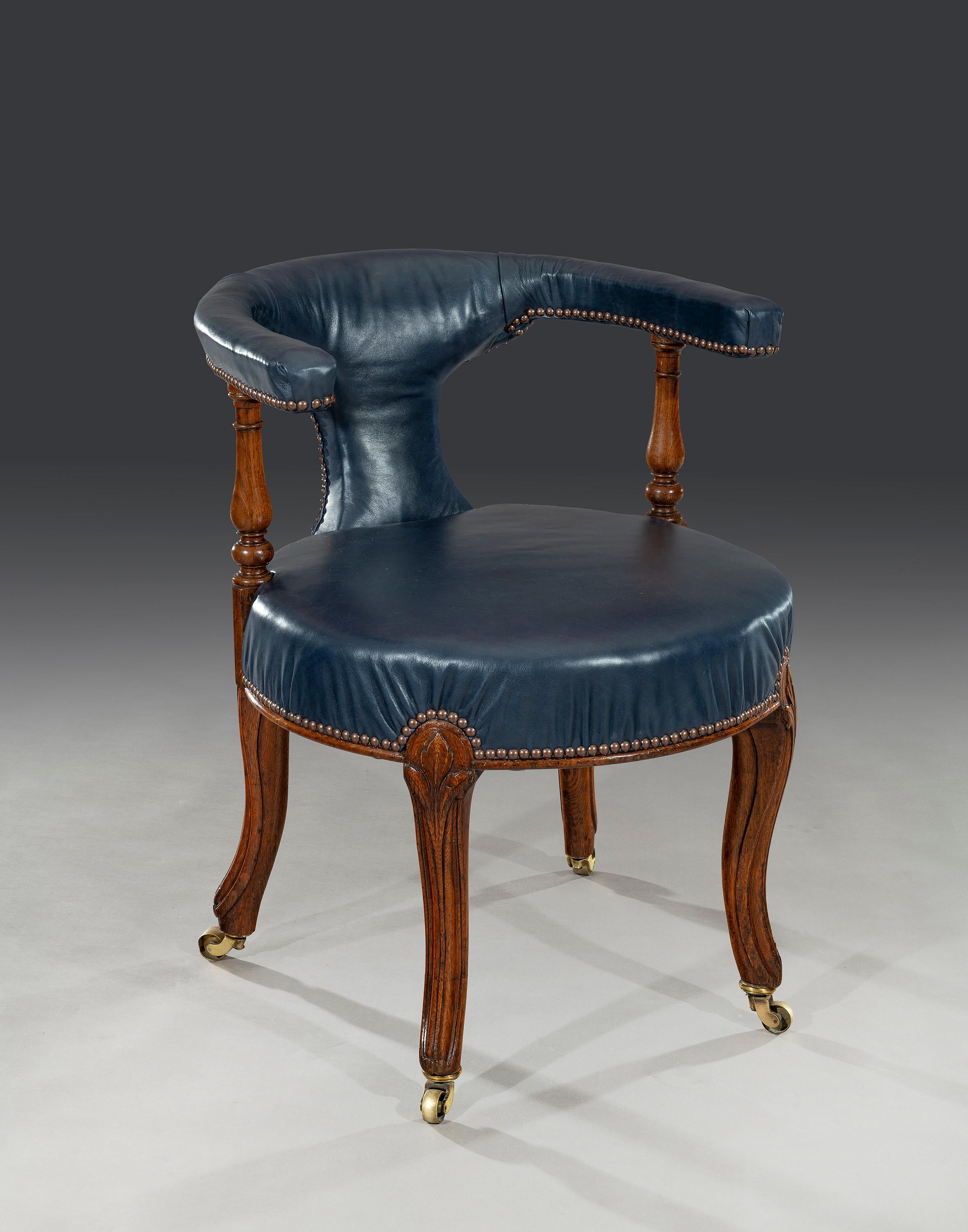 The circular seat is firmly upholstered in a blue leather as is the 'horseshoe' shaped back rail that is supported on turned oak columns. The front legs are carved with some relief decoration with plain shaped legs to the reverse. The leather