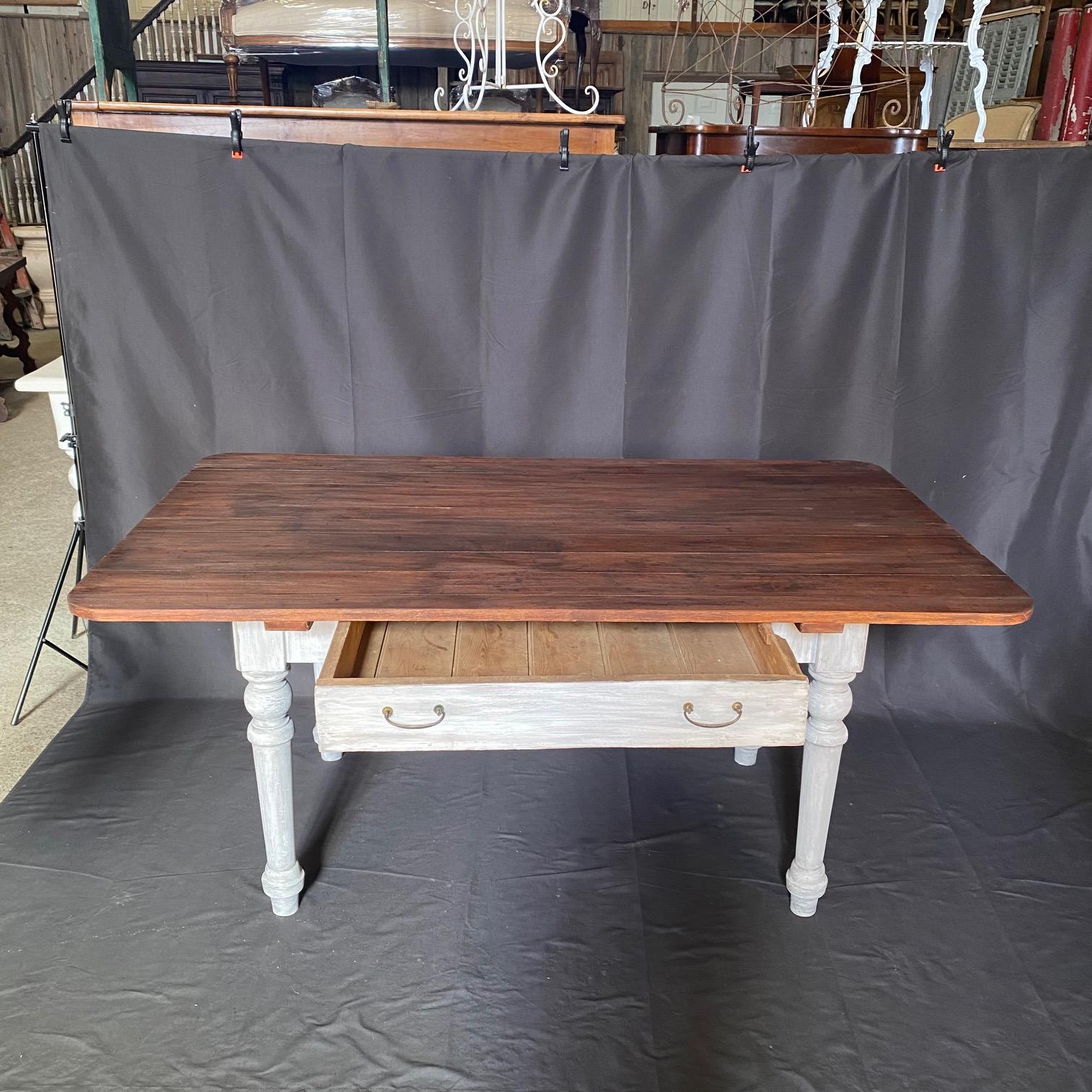 Esta mesa de granja de estilo rural francés fabricada en el siglo XIX tiene un generoso cajón grande con preciosos tiradores originales hechos a mano en el frente. Parte superior recién restaurada e impresionante pintura blanca envejecida en la