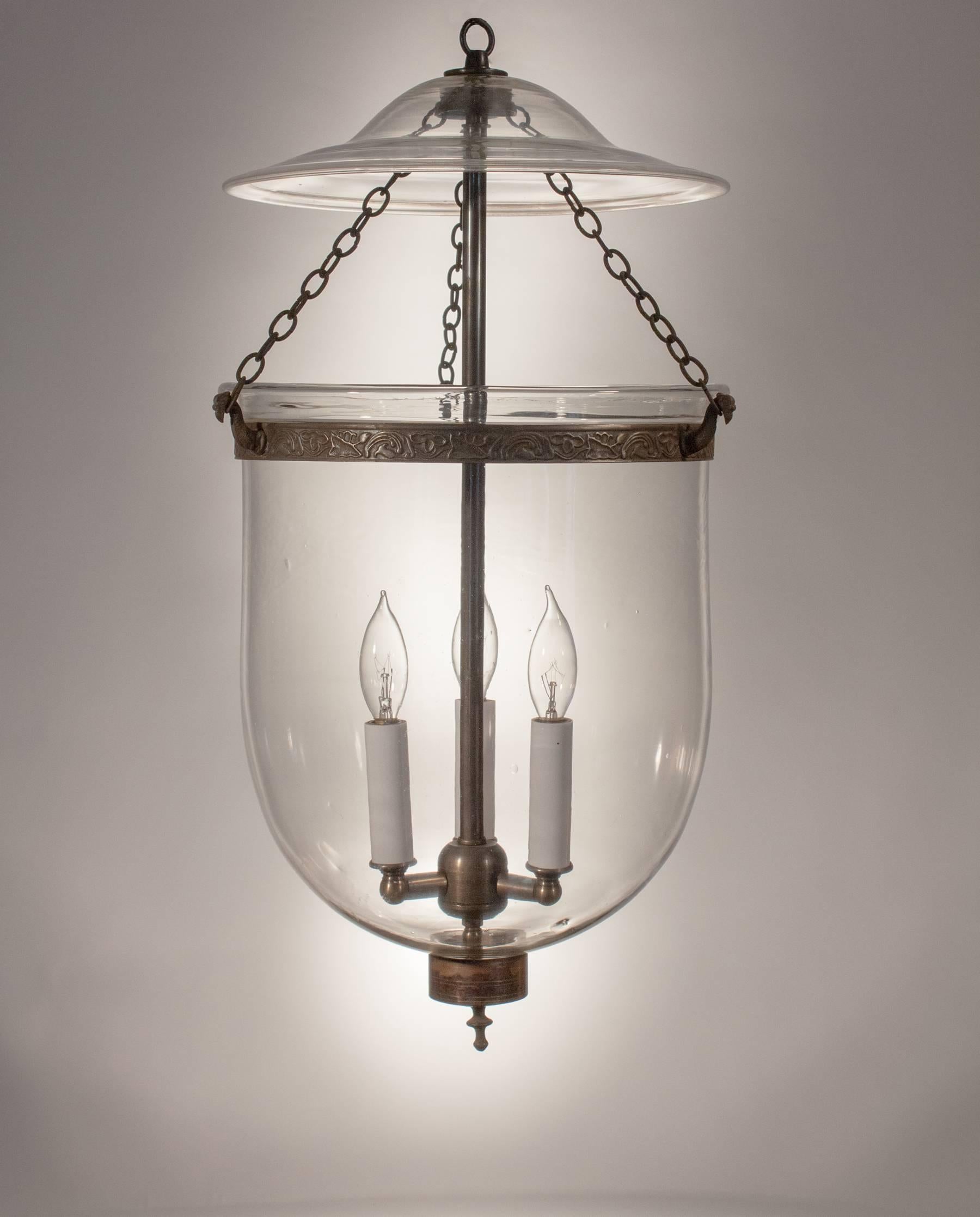 A lovely bell jar lantern from England, circa 1860, with its original smoke bell, brass finial and chains. The embossed brass band, which has been replaced for safety, has a meandering vine design that adds just the right amount of ornamentation to