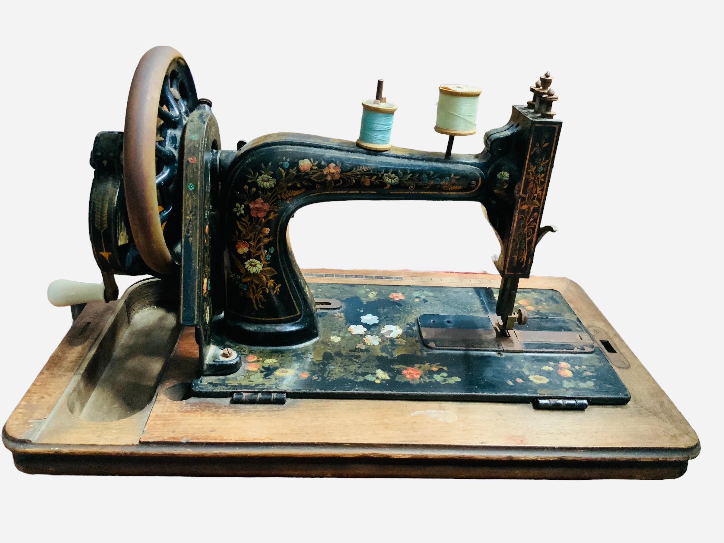 This is a 19th Century Clemens Muller Sewing Machine. It is made of cast iron painted black and adorned with bouquets of flowers decals and mother of pearls like flowers at the lower center part. The sewing machine is attached to a rectangular wood