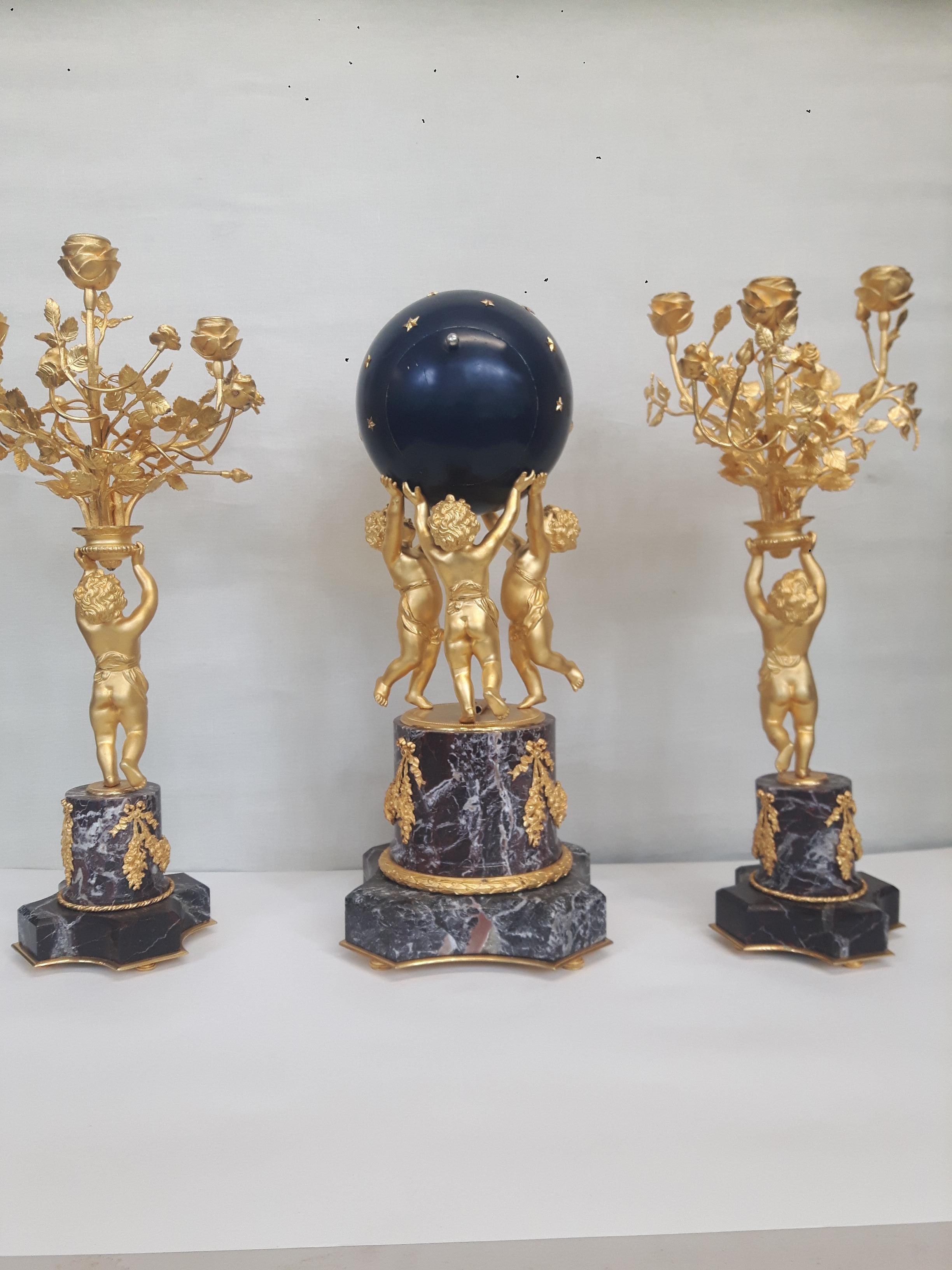 Three piece clock garniture, comprising of a pair of 3 lights ormolou candelabras. Held by cherubs on marble columns, with octagonal bases. The marble applied with finely cast swags. Also roie de blue enamel globe clock, supported by 3 cherubs