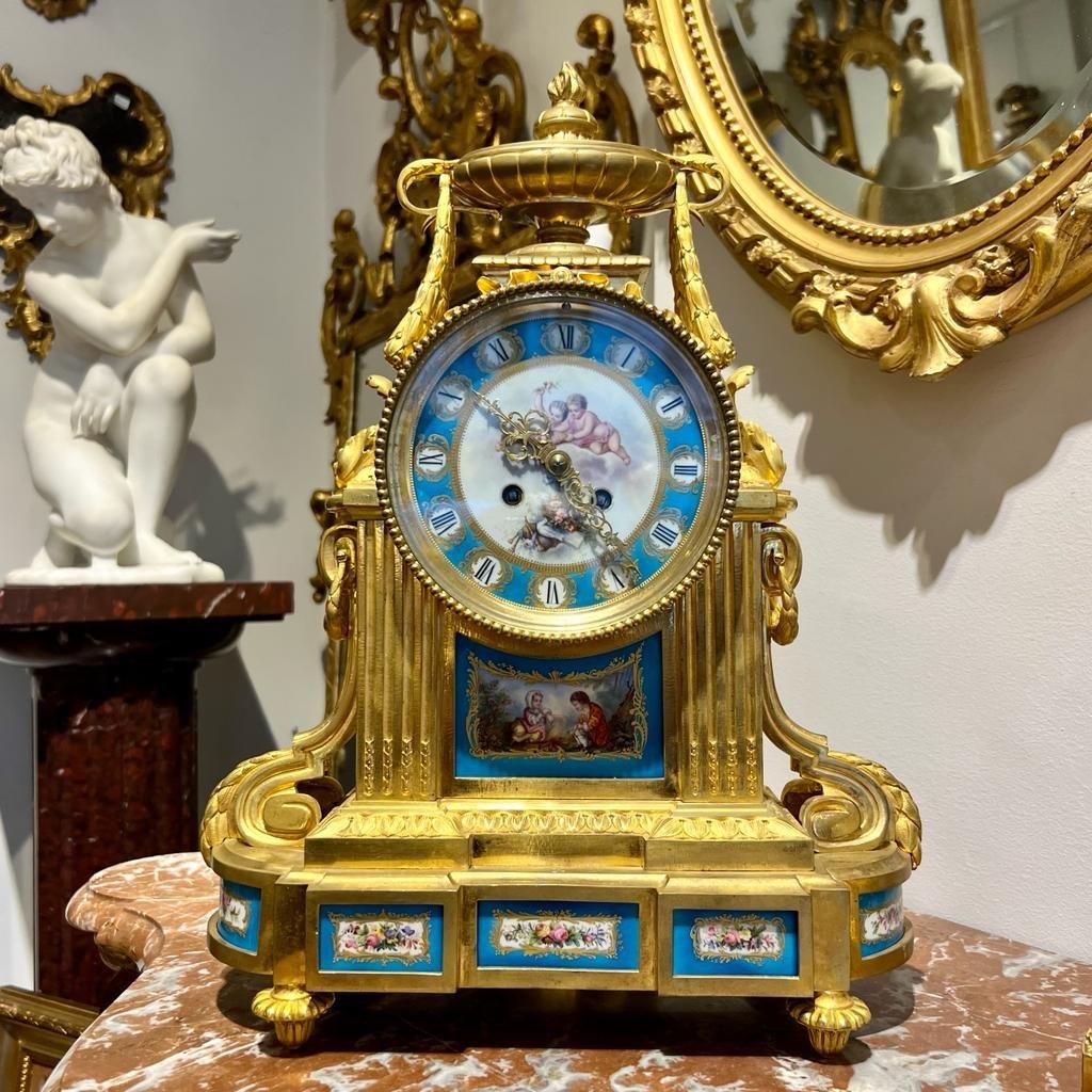 We present you with this stunning mantel clock, designed in the Louis XVI style and originating from the Napoleon III period. It is crafted from gilded bronze and notably adorned with Sévres porcelain plates displaying ornate floral designs on the