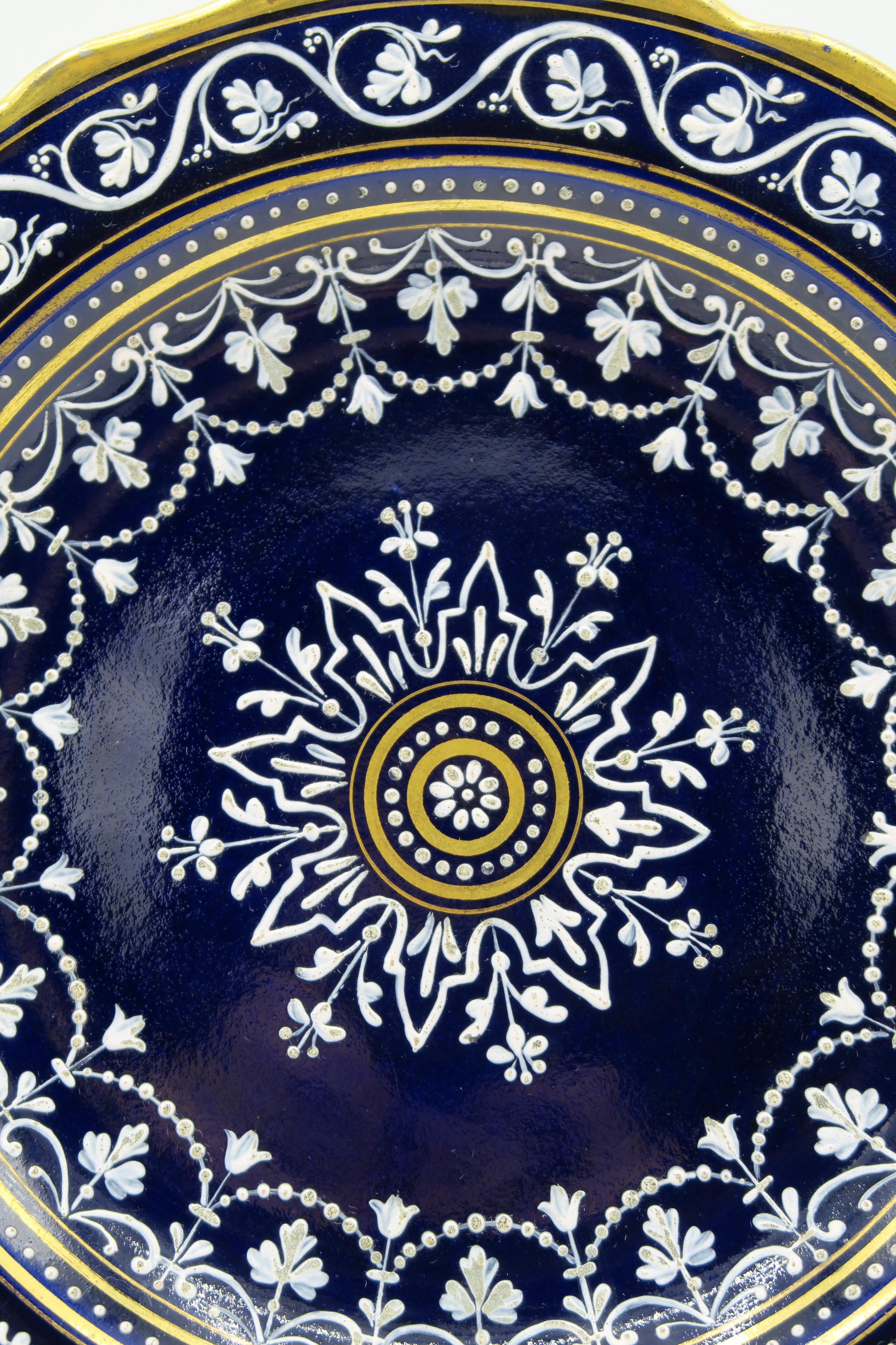 19th century cobalt blue Meissen Praline plate with limoges painting
Cobalt blue background, Gold wavy edges with elaborate “Limoges painting”.
(Slip painting on glaze.)

Leicht ansteigende Fahne, wellenförmiger, goldstaffierter Rand.
