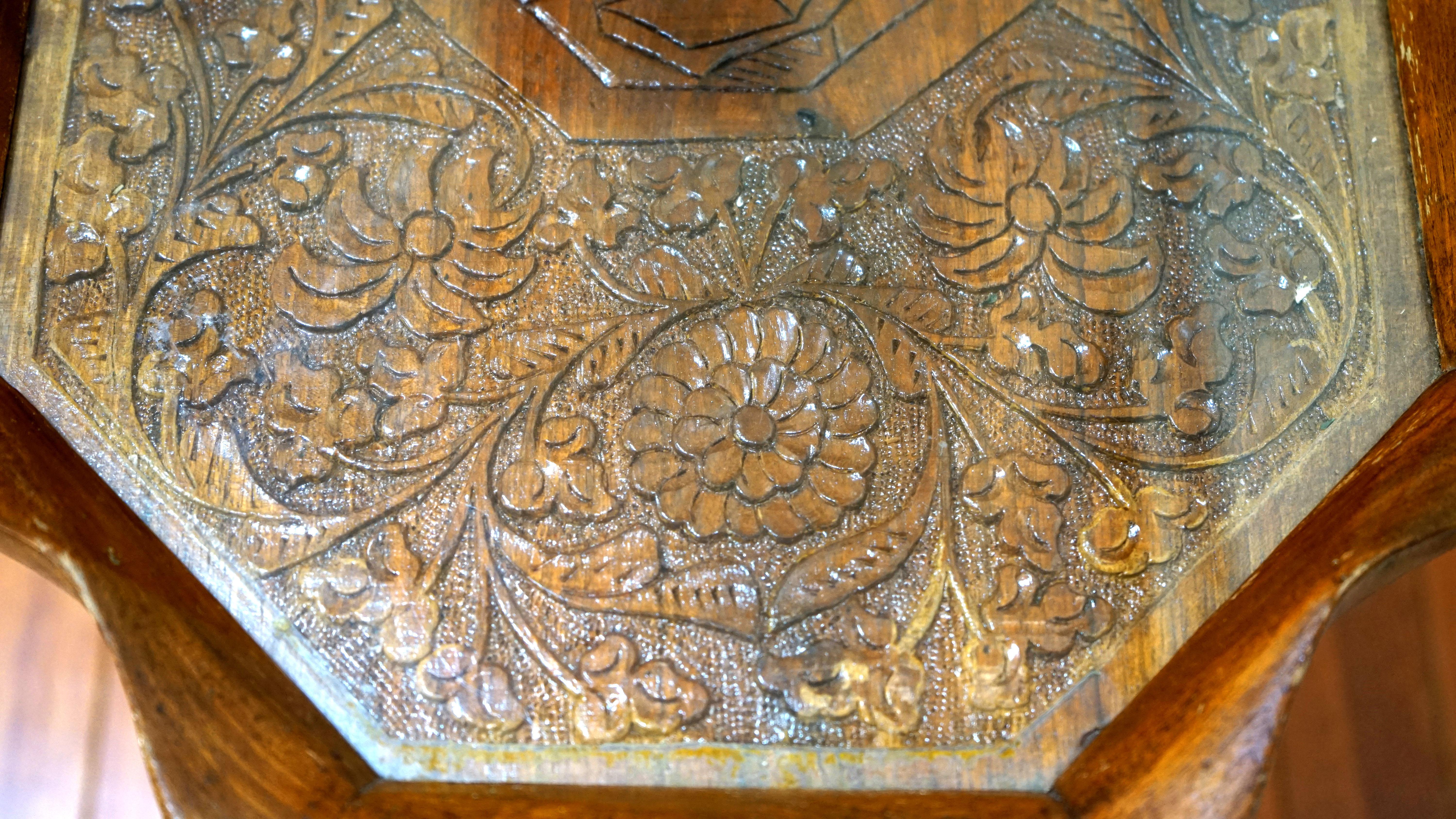 The absolute attraction of this table is the intricate carving on the top, which includes a centerpiece portrait of a gentleman wearing a period hat, and his image is surrounded by hand-carved flowers. It is collectible and functional. It is