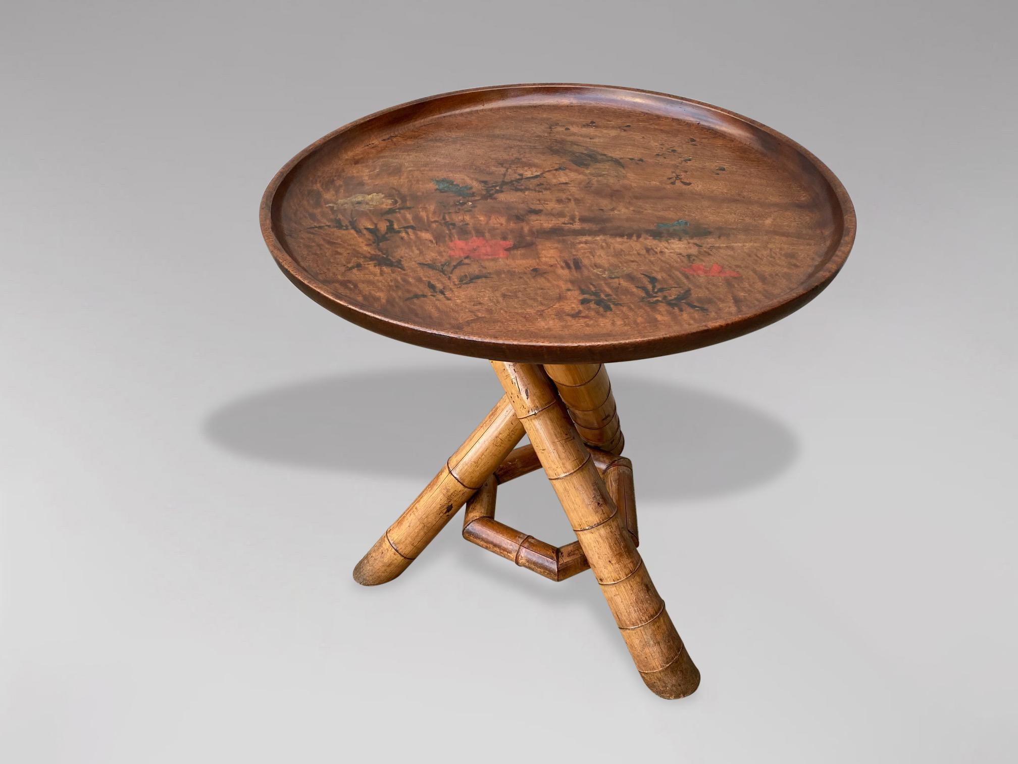 A large 19th century Victorian period Colonial bamboo circular occasional table. A circular dish top in hardwood with beautifully hand painted decorations of a bird, flowers and foliage. Above a bamboo tripod base with twisted leg formation united