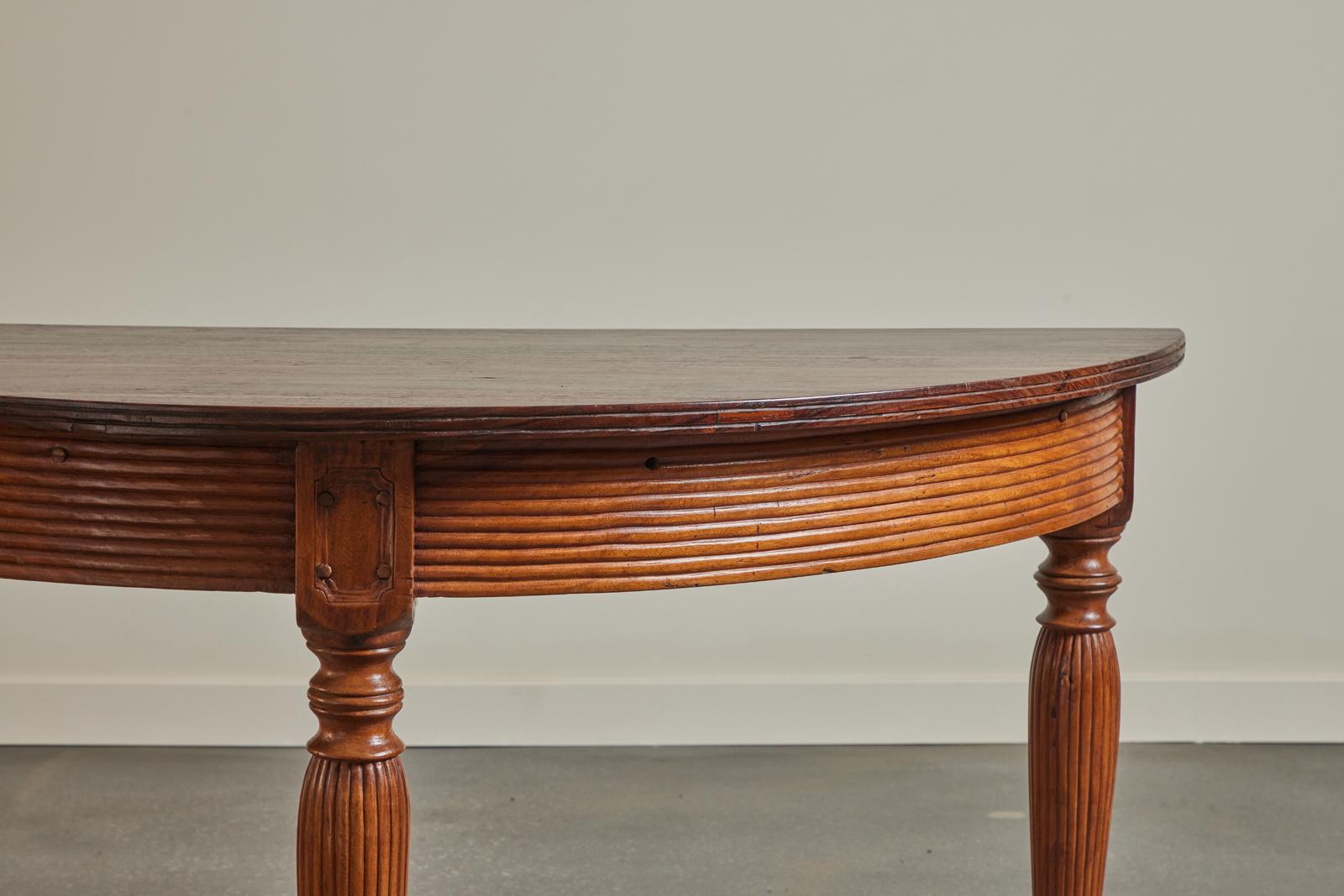 A wonderful 19th century colonial Demi-Lune table made in Indonesia. The legs and apron are teak, fluted and carved on all sides meaning it can be used in the middle of a room. The top is figured Kamagong, a species unique to and highly favored by