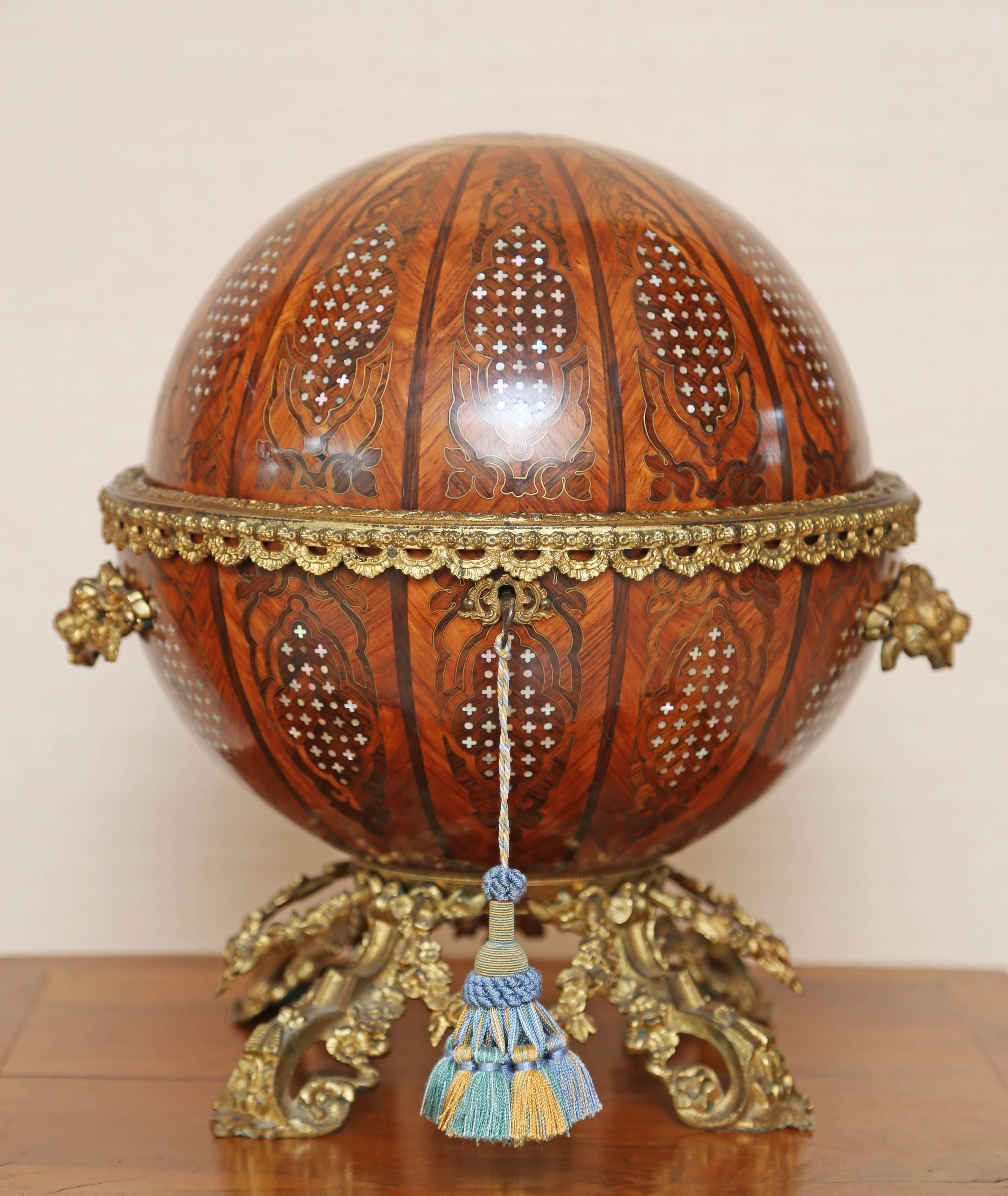 The globular form tantalus with elaborate marquetry decoration incorporating inlaid mother-of-pearl dots and quatrefoils and mounted with gilt-bronze rose garlands as side handles and resting on a base conforming rose-garland festooned base; opening