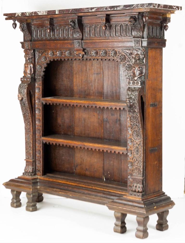 A Continental Renaissance carved oak bookcase from third quarter of 19th century. Surfaced with original variegated marble top resting above a hand-hewn finial, drop mounted lion mask frieze, over a curved arched rosette carved interior rim,
