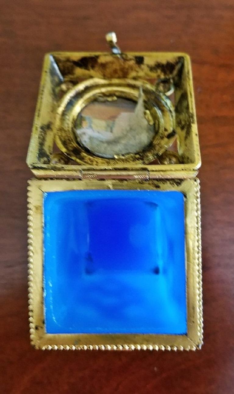 Nice continental ring or pill box from circa 1840. Turquoise blue glass base, gilt metal mounts, with lovely chasing enclosing the glass box.

Hand-painted miniature Palace Scene on plaque and under glass, in the center of the lid (possibly