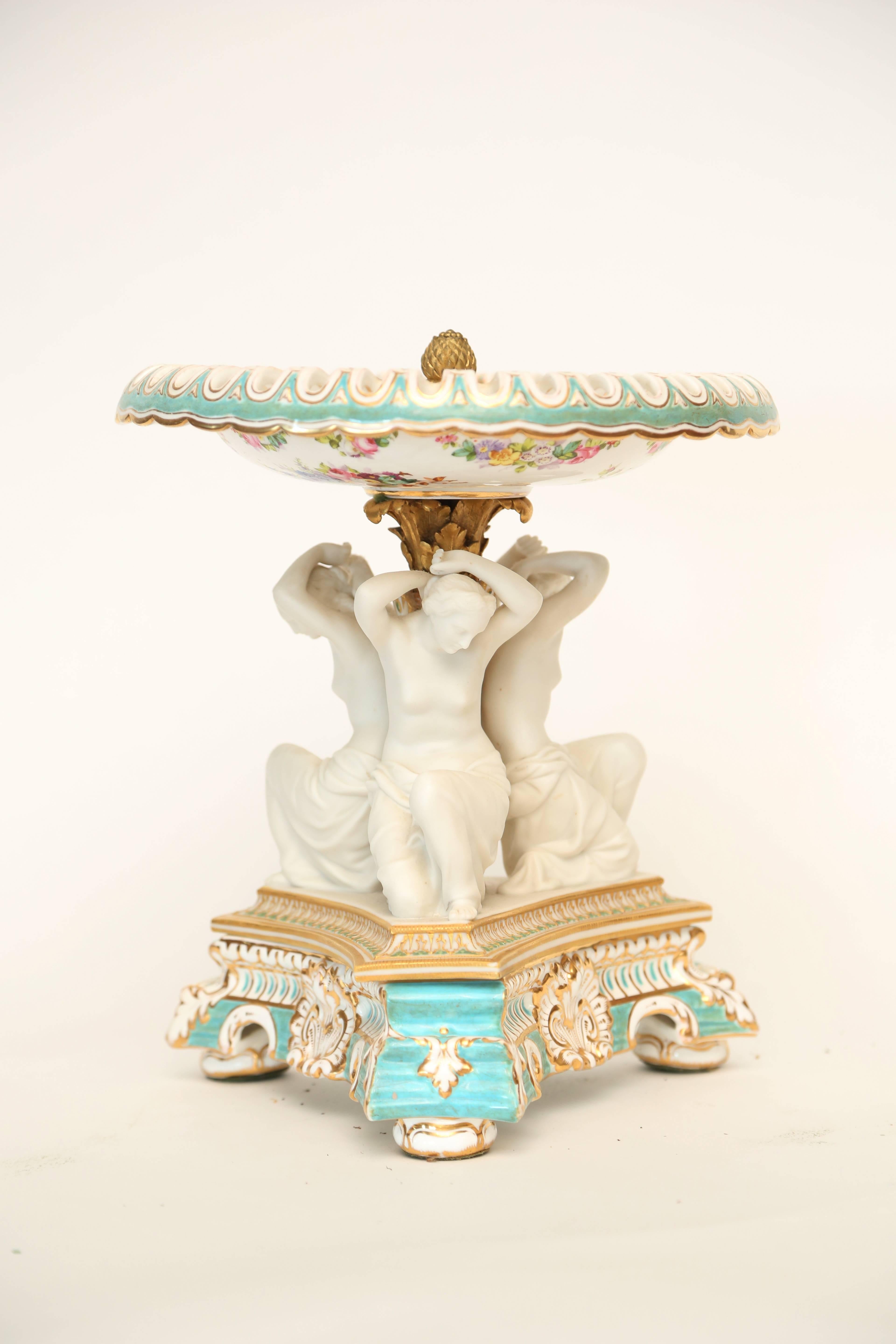 The dish with pierced rim painted with floral festoons above a gilt and aqua blue base molded with shells and scrolls and mounted with three biscuit porcelain figures of kneeling maidens; the top attached to the base with a foliate gilt-metal mount