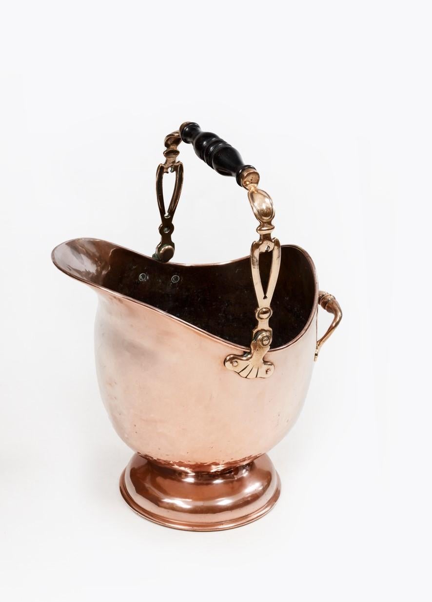 19th Century copper coal scuttle in heavy gauge helmet form standing on a shaped dome base with a turned wood swing top handle & simple side handle.