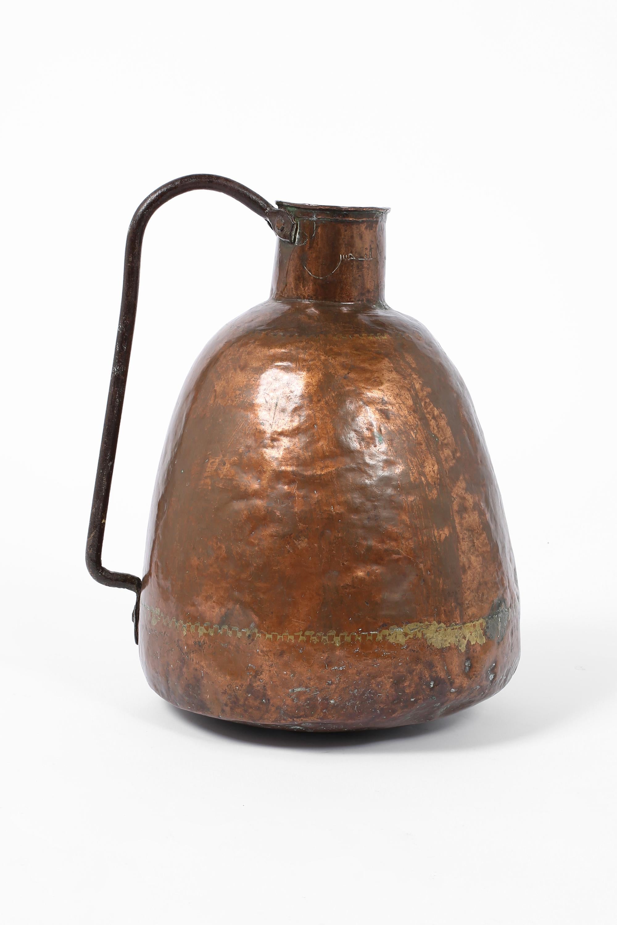 A large, beautifully patinated late 19th century water pitcher or vessel, of dovetailed copper construction with forged iron handle. Indistinctly engraved ??? to the neck, meaning ‘unclean’ in Arabic. Algerian, c. 1890.