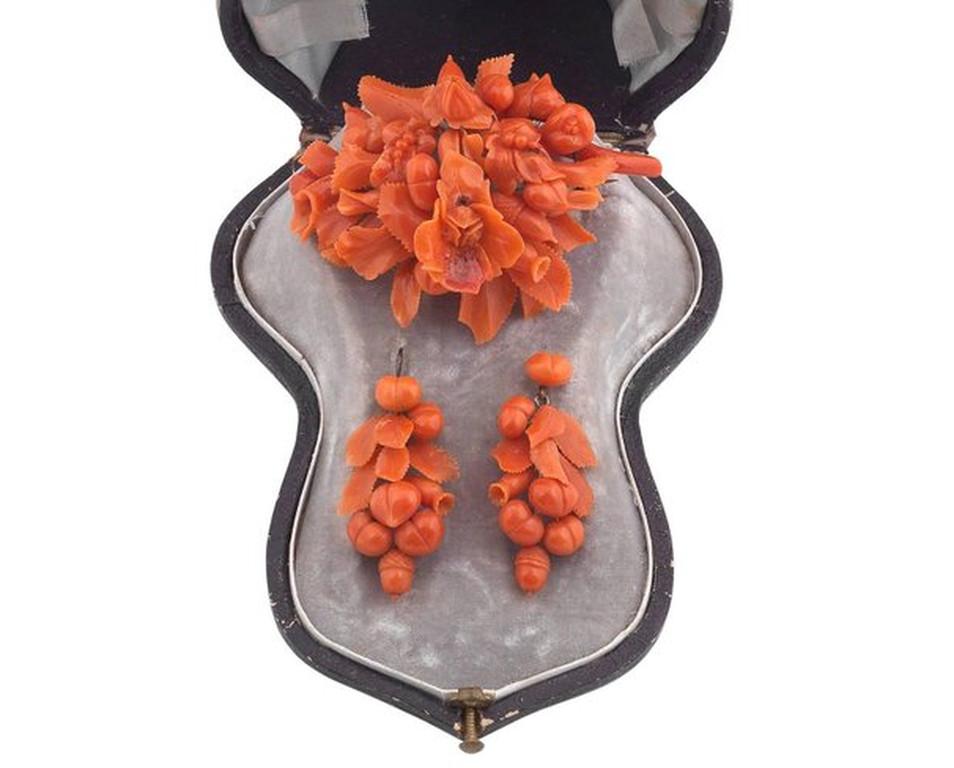 The brooch formed as a series of corals carved as flowers, leaves, buds and berries, the earrings of complimentary design, to hook fittings, brooch width 56mm, earring length 40mm, to a fitted case 