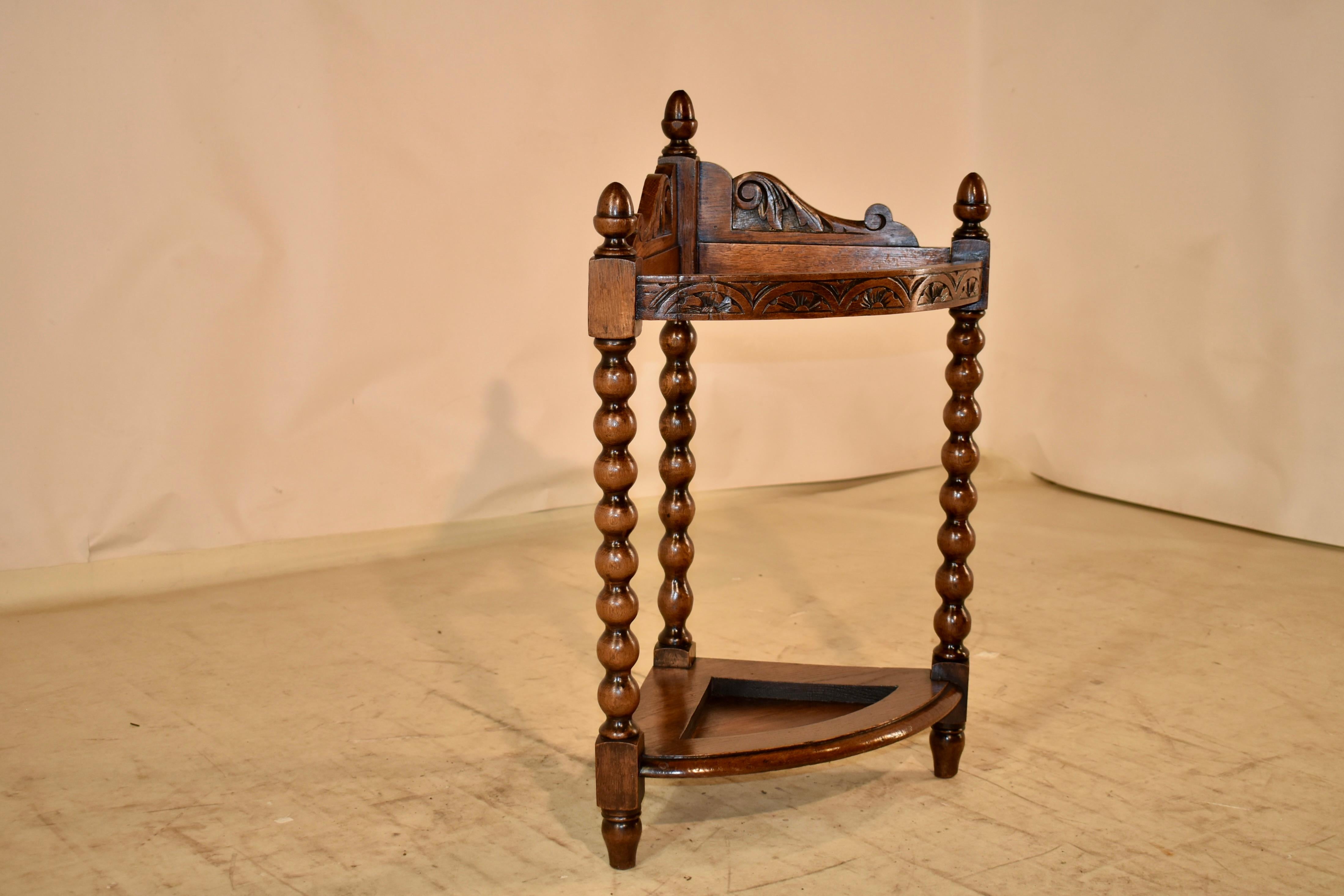19th century oak corner walking stick stand from England.  The top has a scalloped and hand carved decorated back, decorated further with hand turned finials for additional design interest.  The front rail is curved in a convex shape and is hand