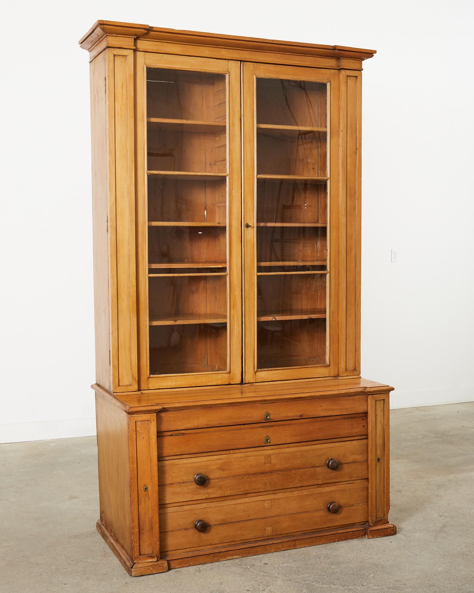 Unique 19th century country English library bookcase or cabinet crafted from fruitwood. The tall two-part case has a six shelf bookcase on the top featuring glazed doors. The bookcase is topped with a cornice molding. The bottom case is fronted by