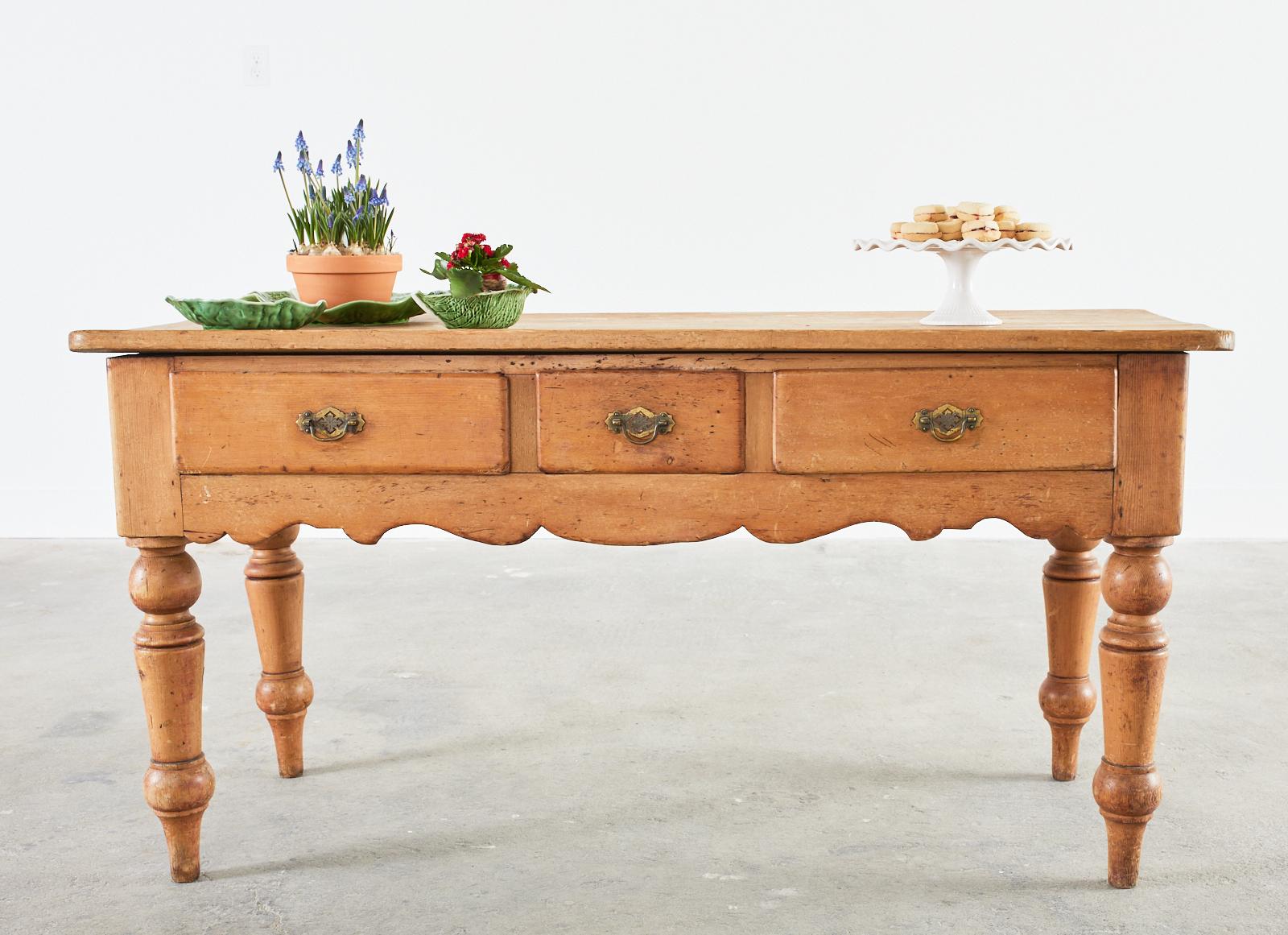 Charming 19th-century country English provincial farmhouse work table, console, or sideboard crafted from pine. This kitchen workhorse has a 1 inch thick plank top and is fronted by three storage drawers with brass pulls above a shaped apron.