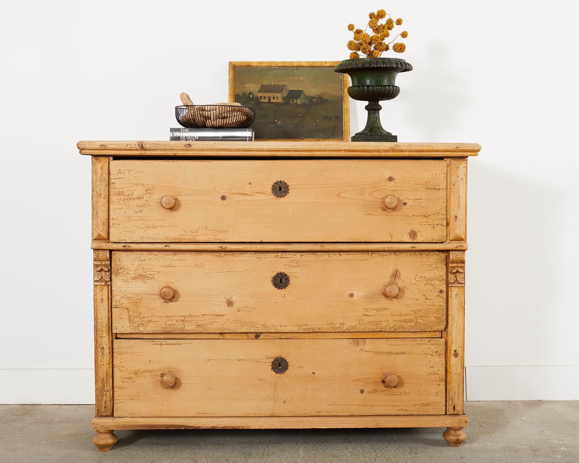 Grand 19th century country English provincial chest of drawers or commode crafted from thick pine boards. The pine has a desirable aged and distressed patina with prior insect damage and wear on the finish. The chest is fronted by three large