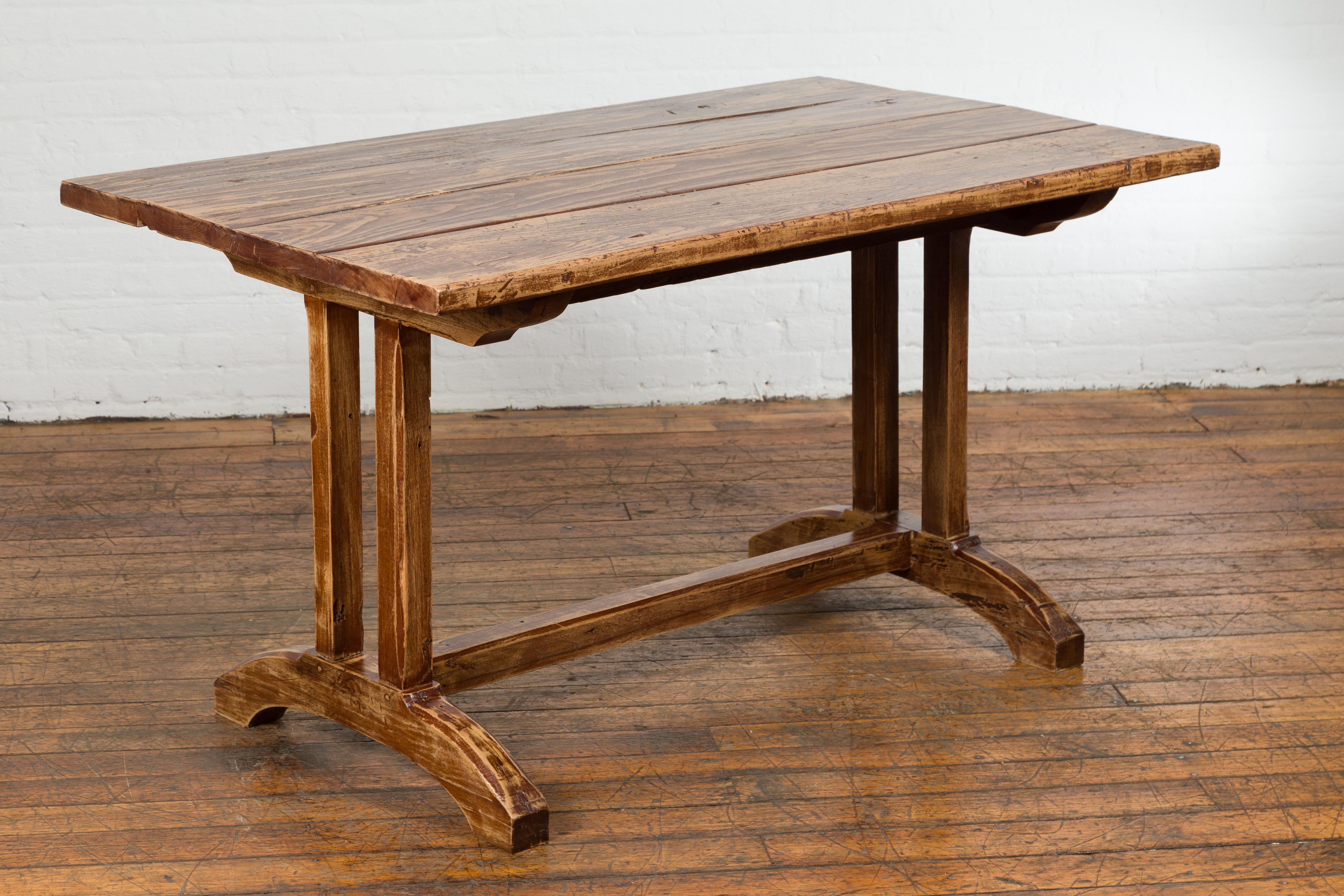 A rustic farmhouse table from the 19th century with trestle base and custom distressed finish. Emanating timeless charm from the 19th century, this rustic farmhouse table is an ode to authenticity and craftsmanship. Boasting a robust trestle base,