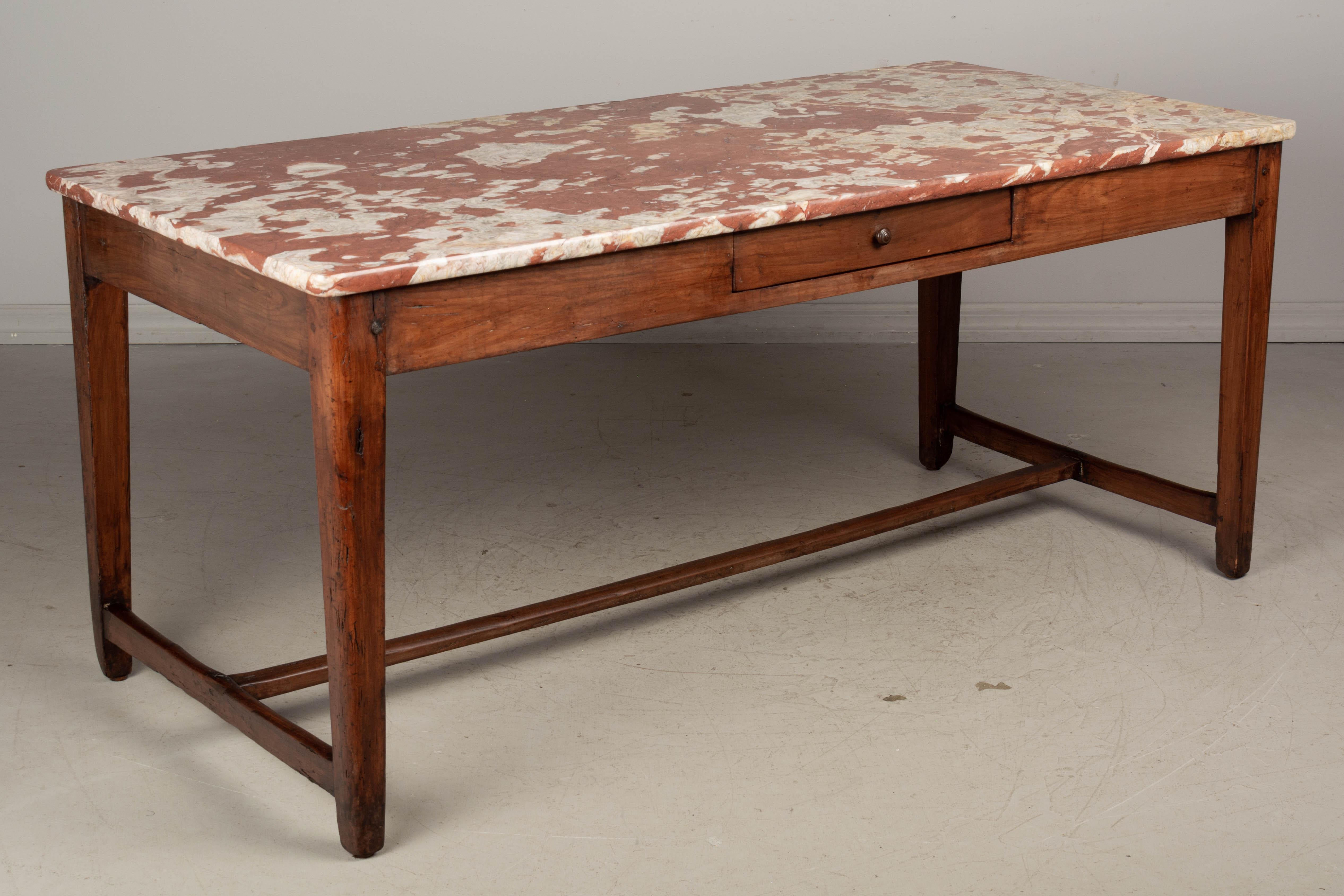 A 19th century French table made of solid cherry wood with beautiful Rouge Royale marble top. Sturdy pegged construction with tapered legs and stretcher. Two dovetailed drawers with divided interior. Waxed finish. This farm table sits lower than