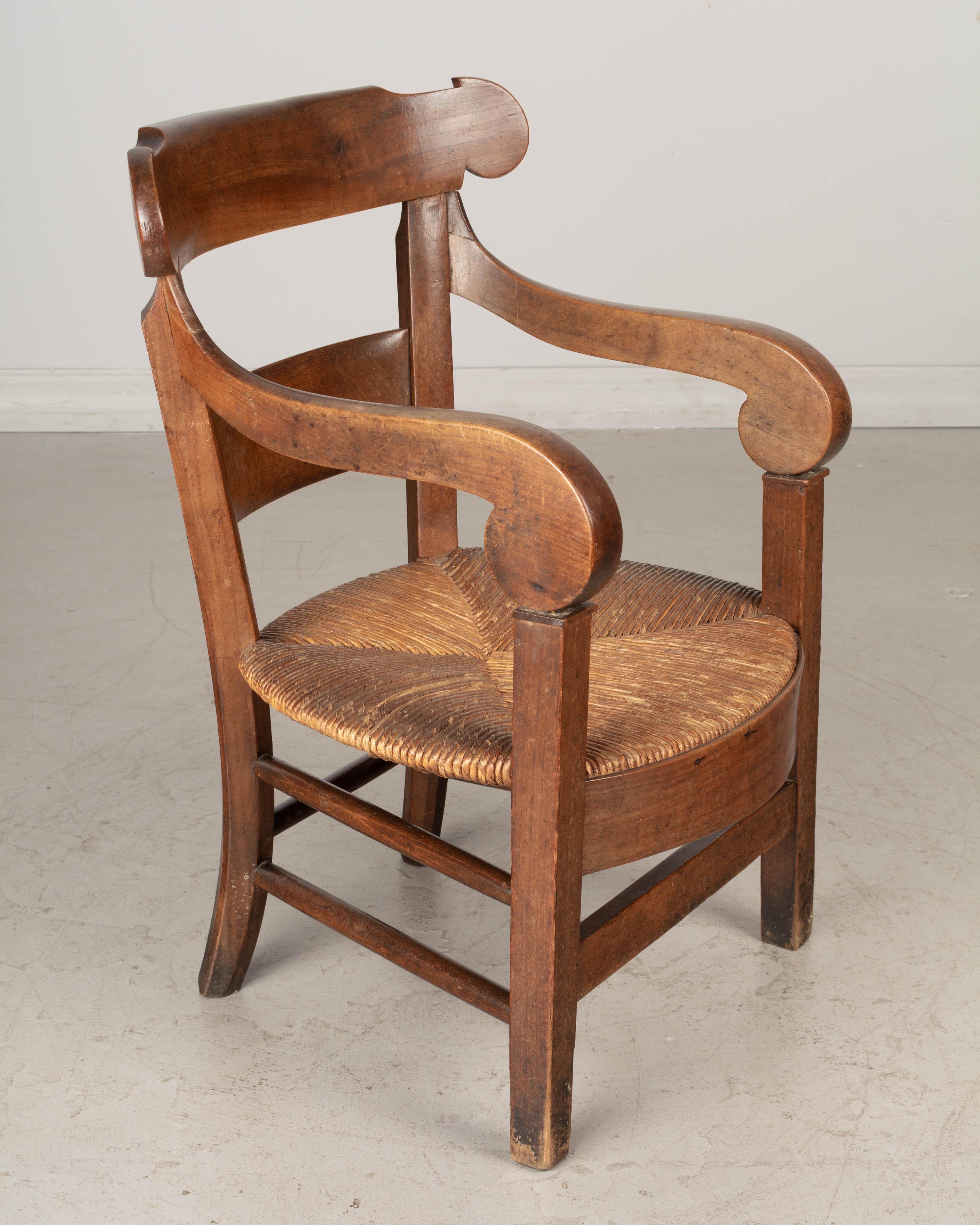 A 19th century Country French child size chair hand crafted of solid walnut with large scrolled arms and natural rush seat. Waxed patina. Good and sturdy.
