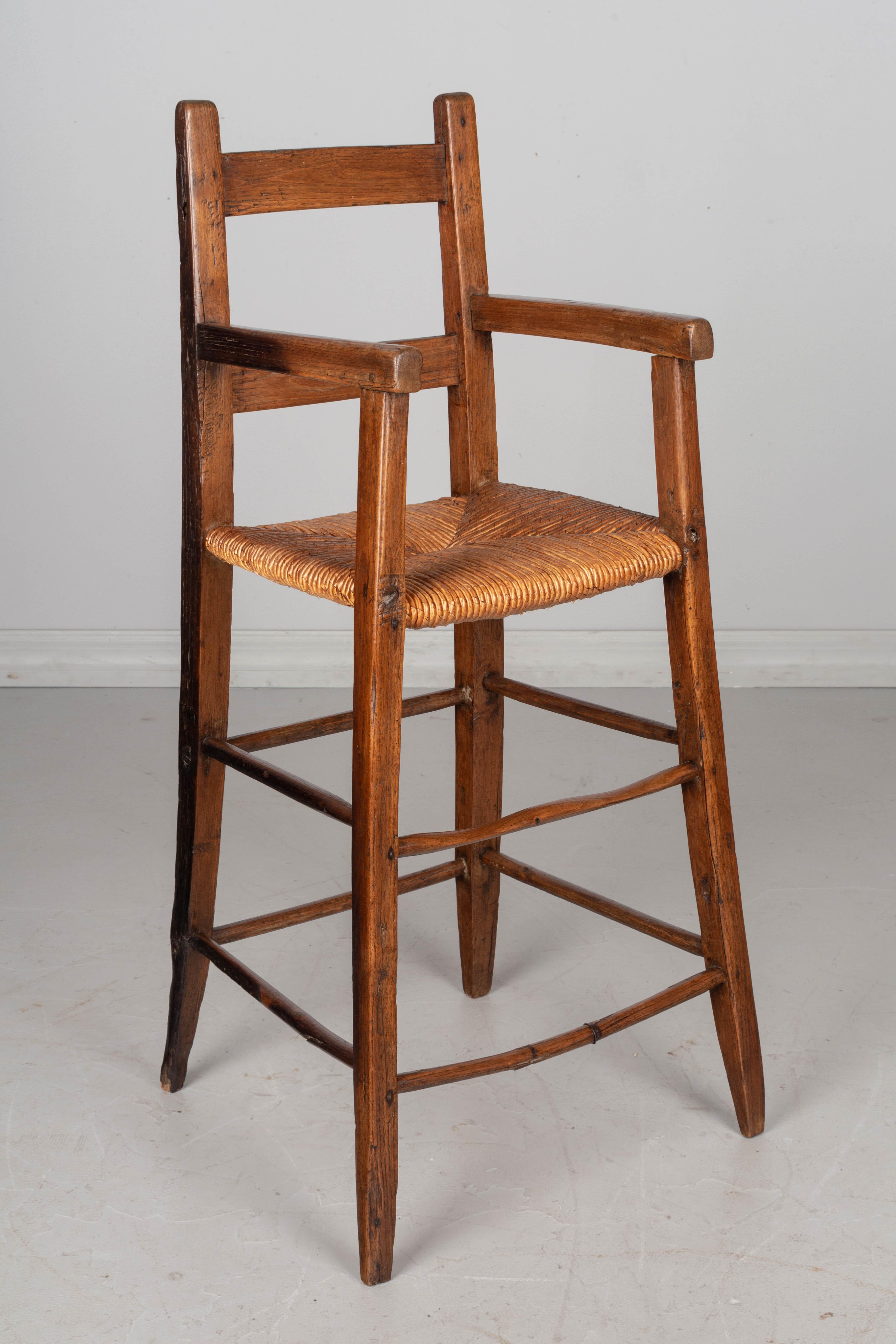 A late 19th century Country French child's high chair, or doll chair, made of oak with waxed patina and natural rush seat. The spindles are all original, some have been repaired. Wood is darkened on one side, may have been used next to a fireplace.