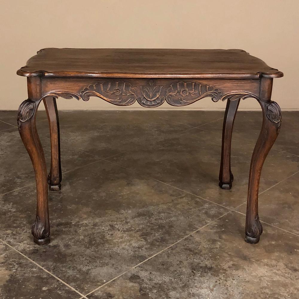 19th Century Country French end table was meticulously hand-crafted from dense, old-growth oak, and features a beautifully contoured and beveled top resting on an apron that has been scrolled and hand-carved with foliate and floral motifs on all