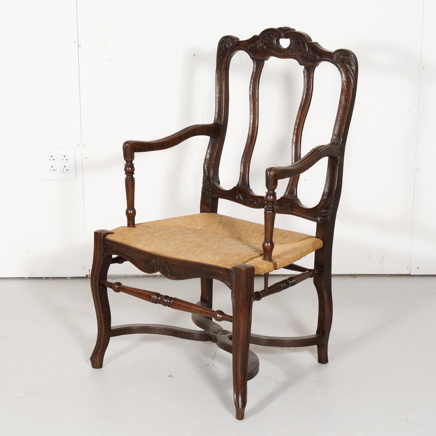 A 19th century Country French hand carved oak rush seat armchair, circa 1880s. This provincial armchair features carved floral motifs on the crest rail and apron with curved armrests. Raised on cabriole legs joined by carved X-stretcher. A wonderful