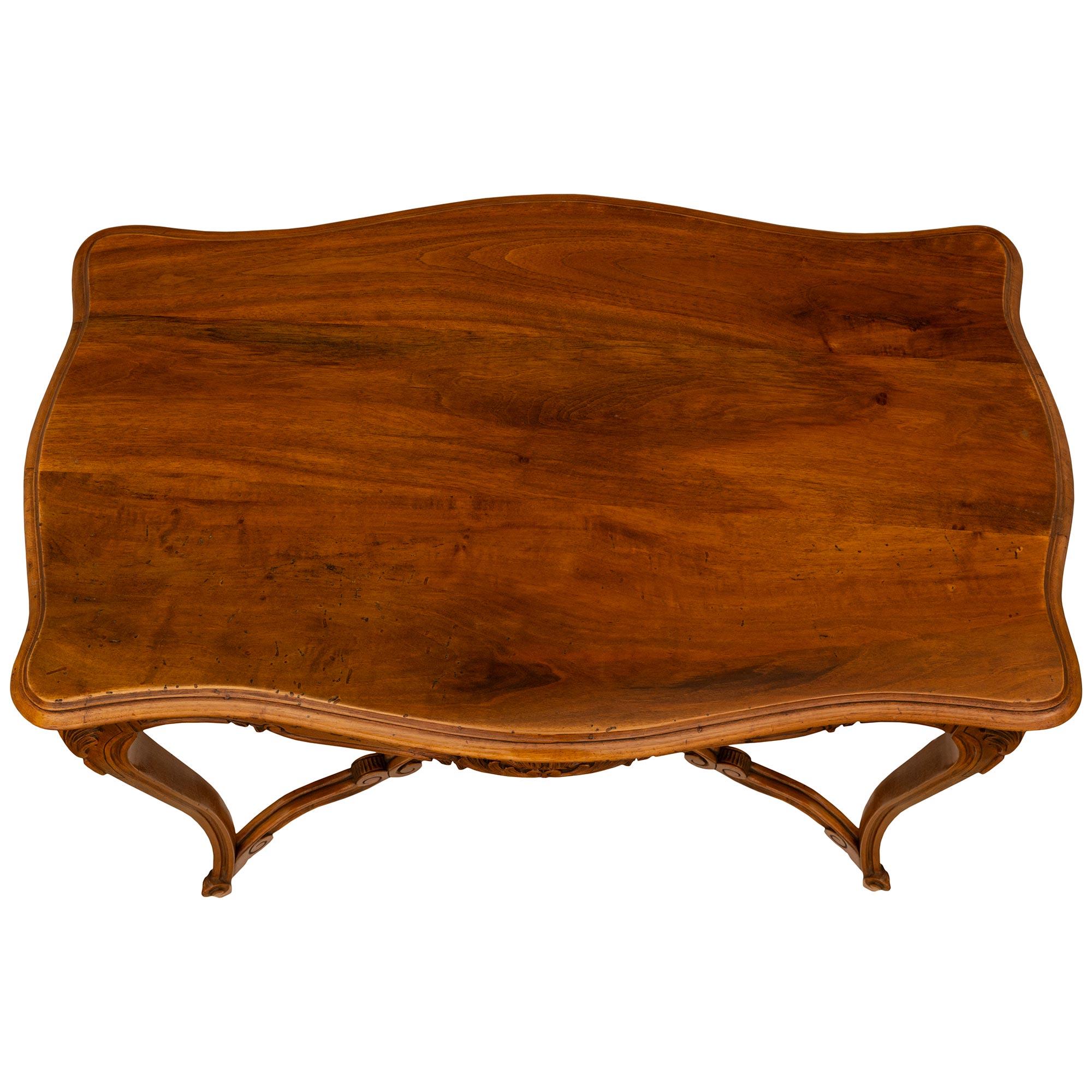 A fine 19th century Country French Louis XV st. honey colored cherry wood side table. The table is raised on carbiole legs topped with acanthus leaf carvings. The legs are joined by scrolled X stretcher centered by an urn with finial. At the